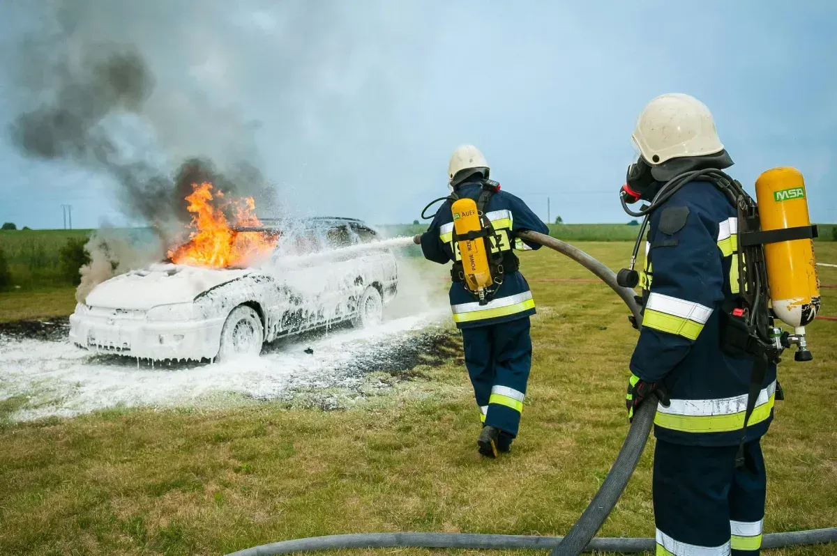 Bomberos extinguiendo un incendio de coche con espuma en un campo.