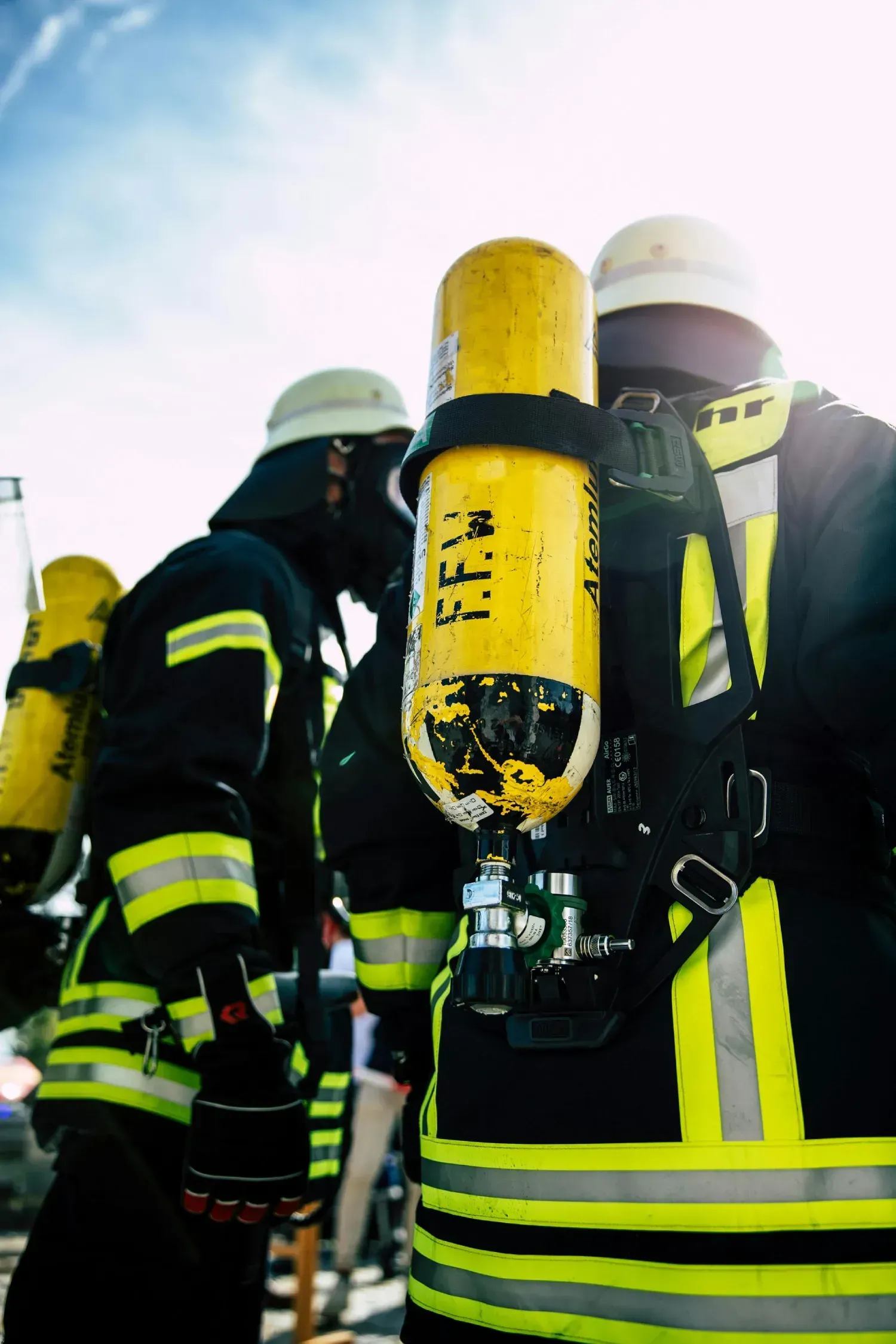 Bomberos con equipo de protección, incluyendo tanques de oxígeno, frente a un cielo azul.