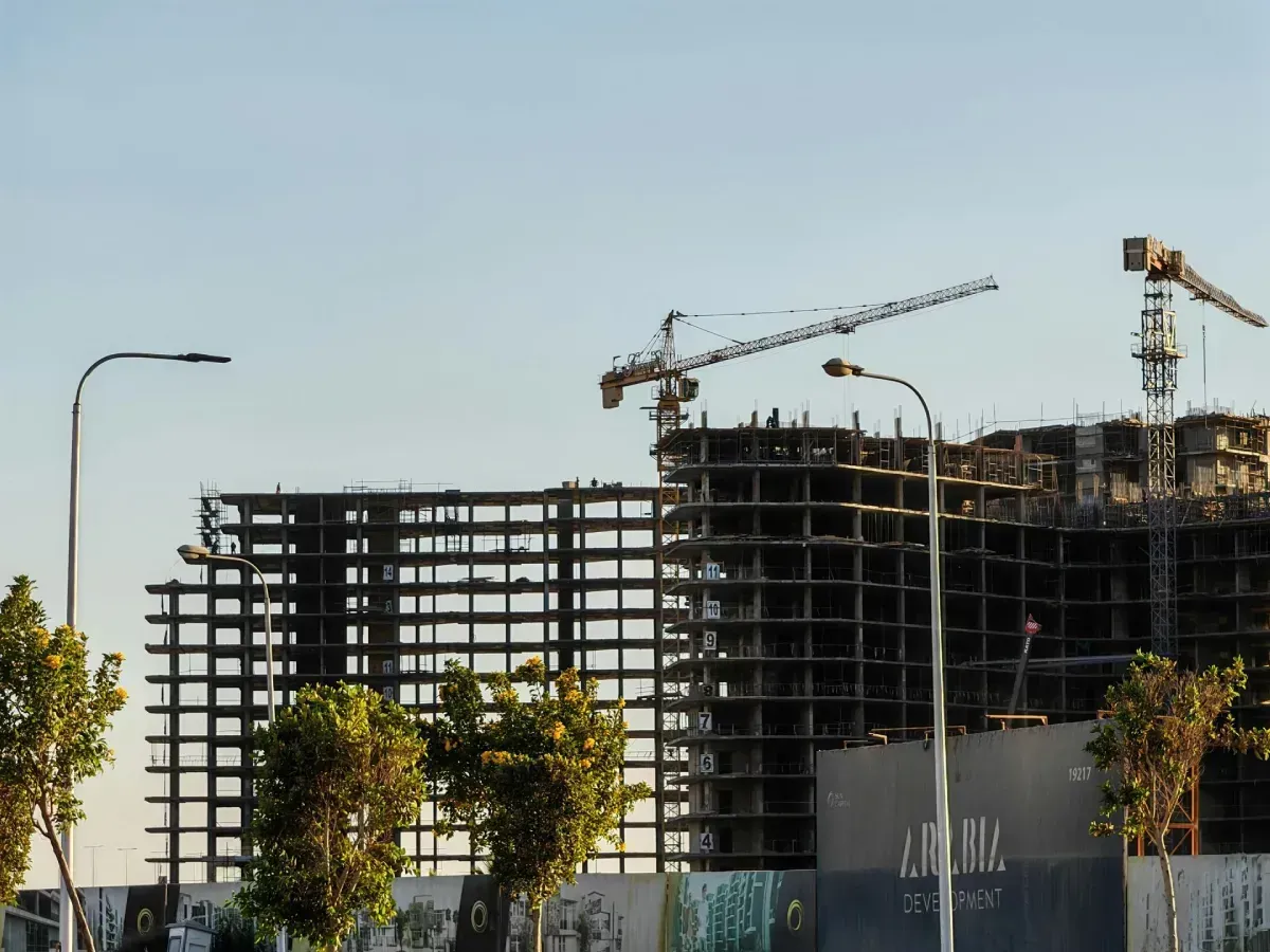 Zona en construcción con altos edificios en construcción y grúas contra un cielo azul.