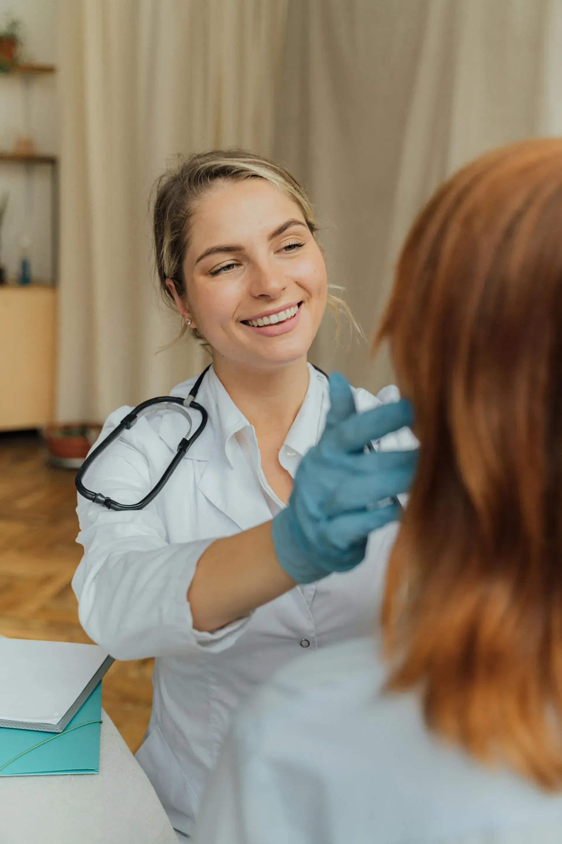 Médico con bata blanca examinando la garganta del paciente, sonriendo, con guantes azules.