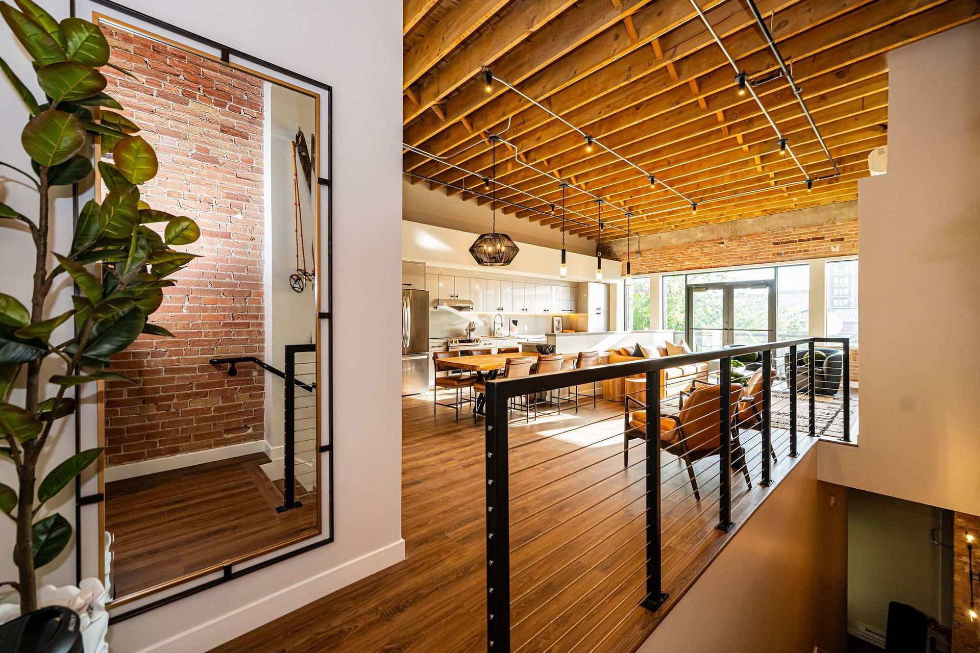Modern loft interior: exposed brick, wooden ceiling, open kitchen, balcony with seating.