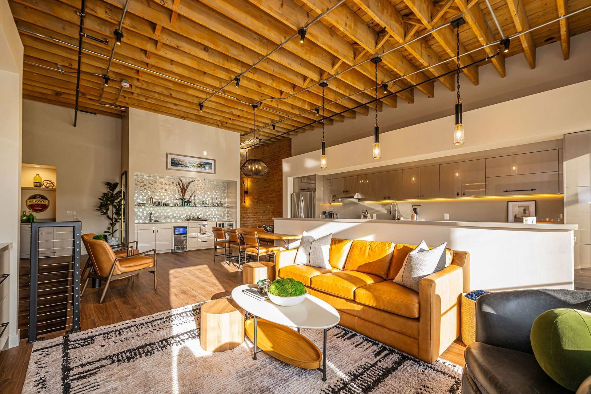 Living room with exposed wooden ceiling, orange sofa, rug, and kitchen in the background.