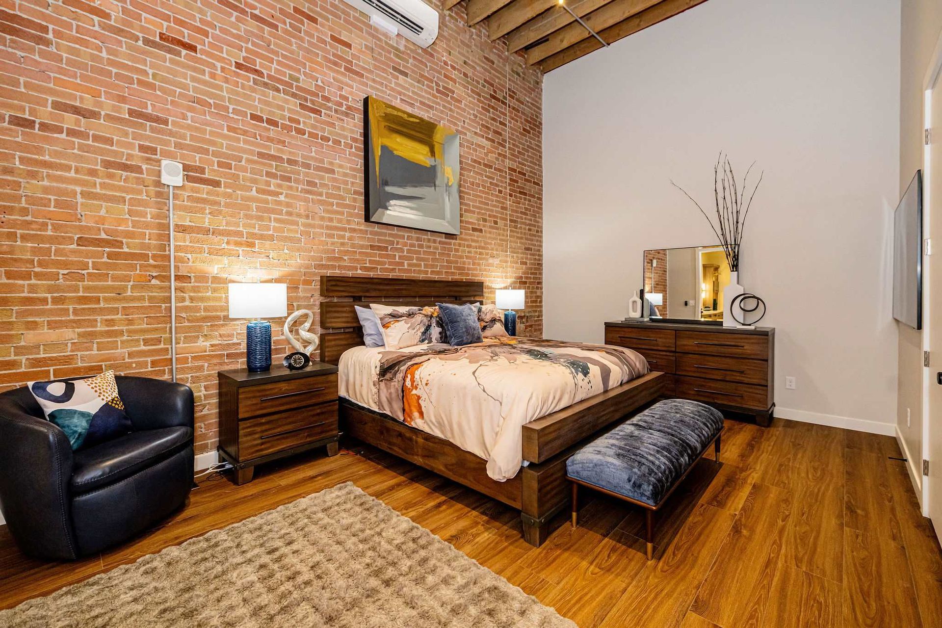 Bedroom with exposed brick wall, wooden furniture, bed, seating, and art.