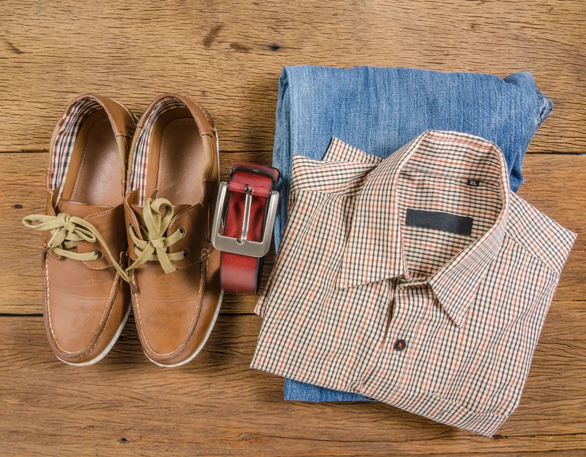 Un par de zapatos, un cinturón, una camisa y unos vaqueros están sobre una mesa de madera.
