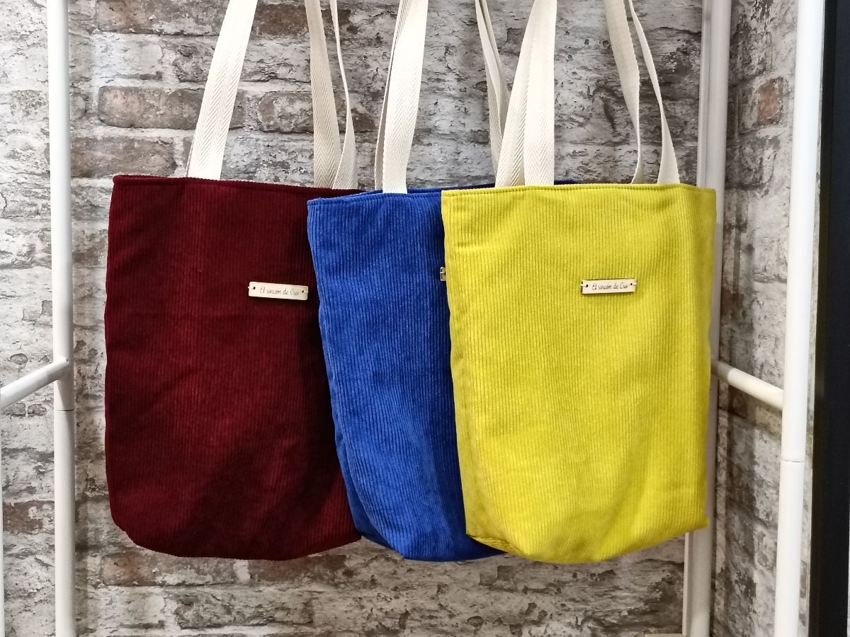 Tres bolsas de mano cuelgan de un estante frente a una pared de ladrillos.