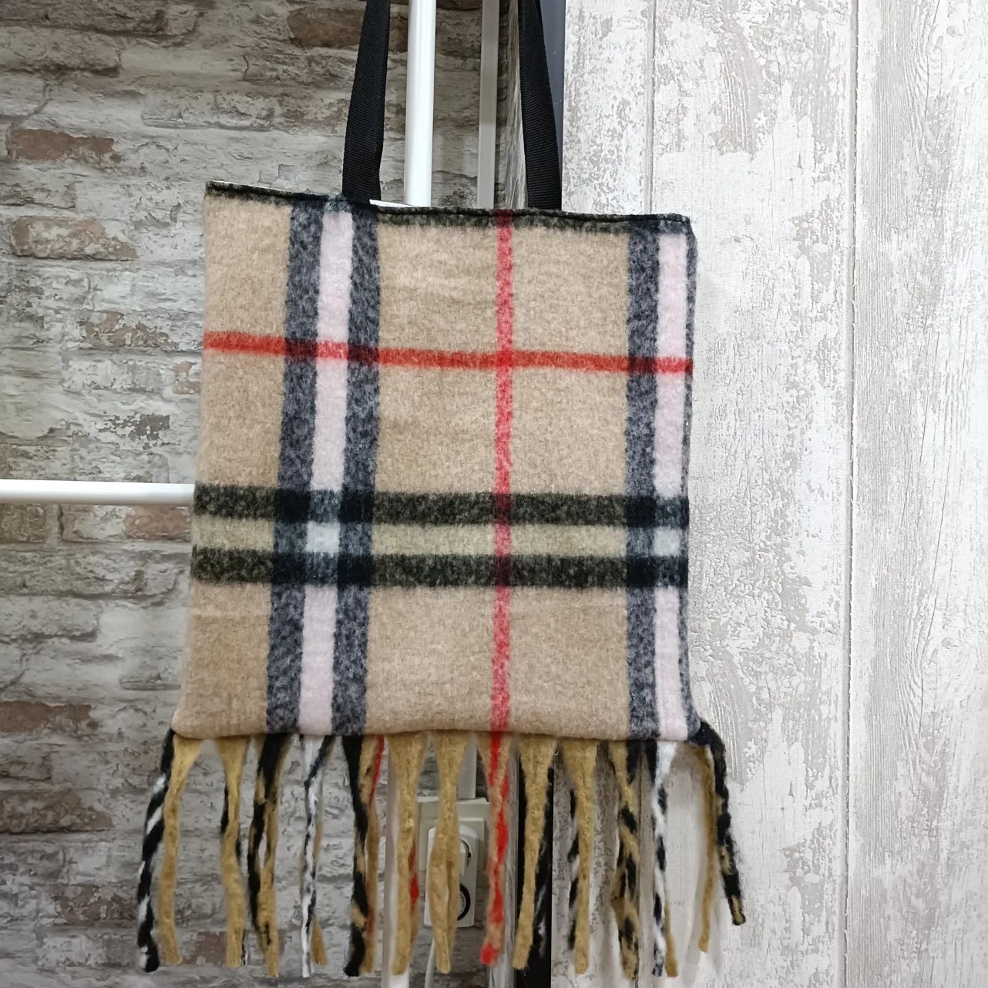 Un bolso de mano a cuadros con flecos cuelga de un poste.