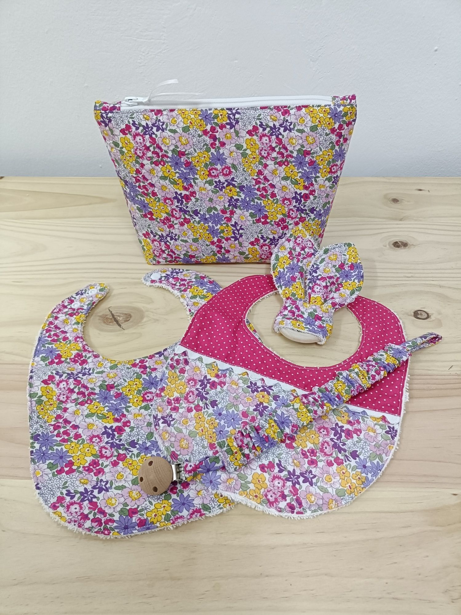 Un babero de bebé, un porta chupete y un bolso están sobre una mesa de madera.