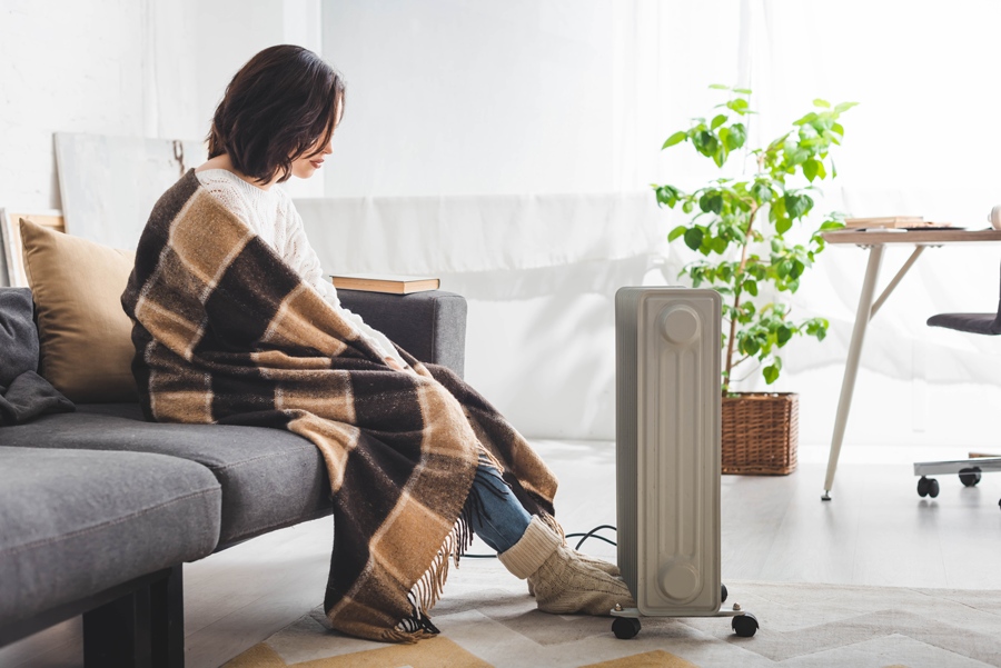 Femme assise sur un canapé devant un radiateur électrique