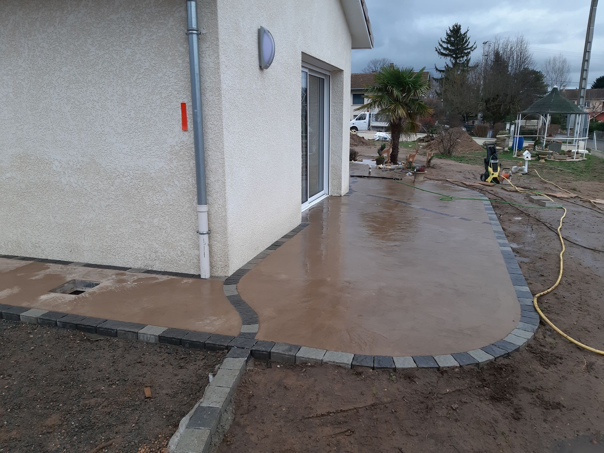 Allée en béton mouillée autour d'une maison aux contours arrondis et cour boueuse après la pluie