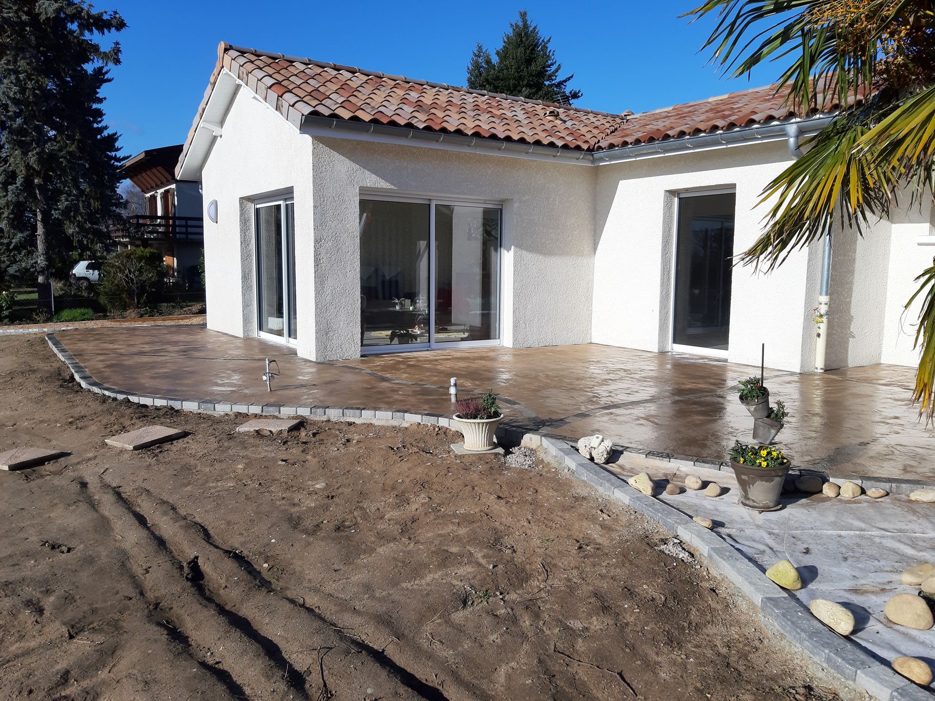 Maison blanche en construction, avec toit de tuiles et terrasse, entourée de terre et de pierres d'aménagement paysager.