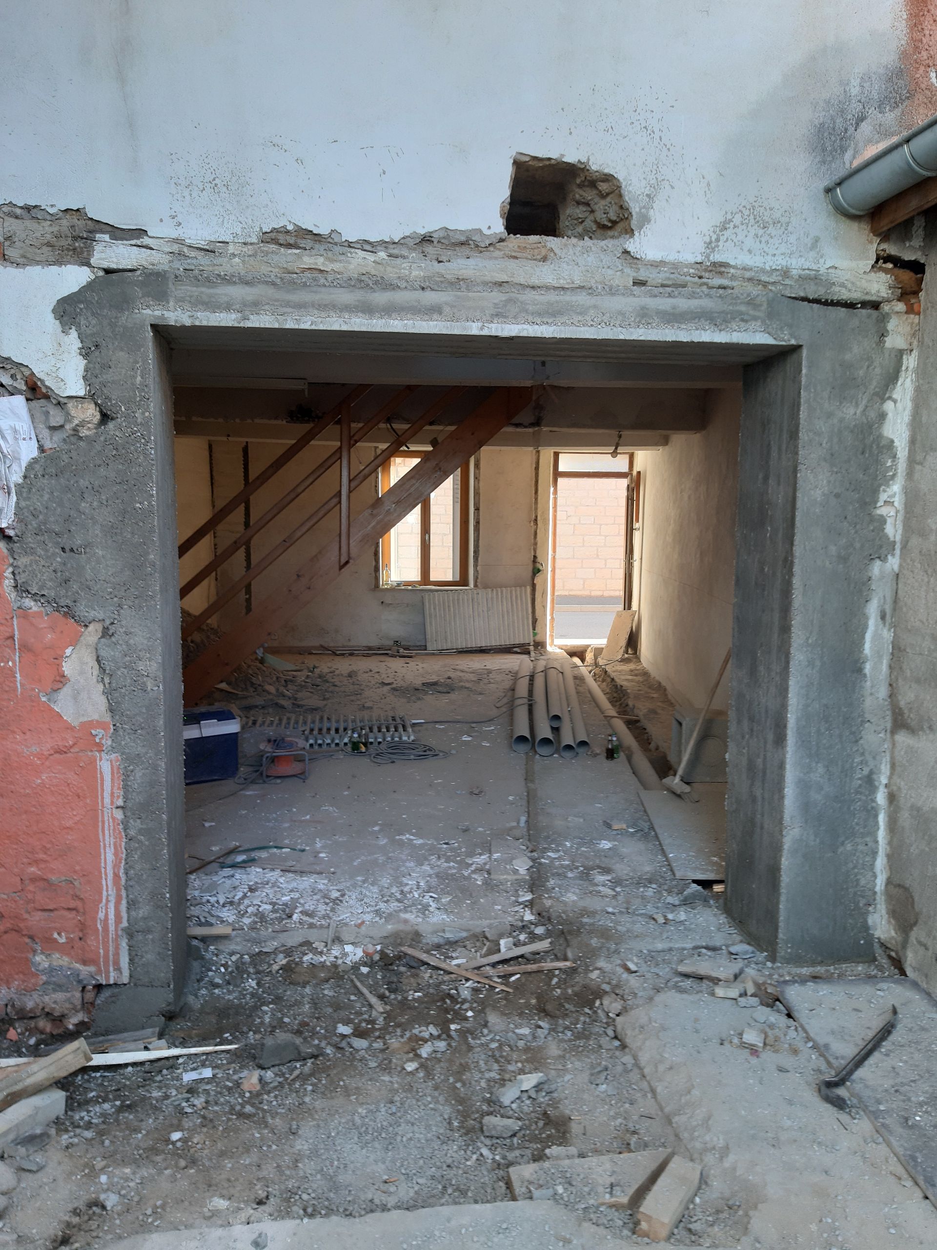 Entrée d'un bâtiment endommagée avec des décombres, des escaliers apparents et une pièce intérieure partiellement ouverte