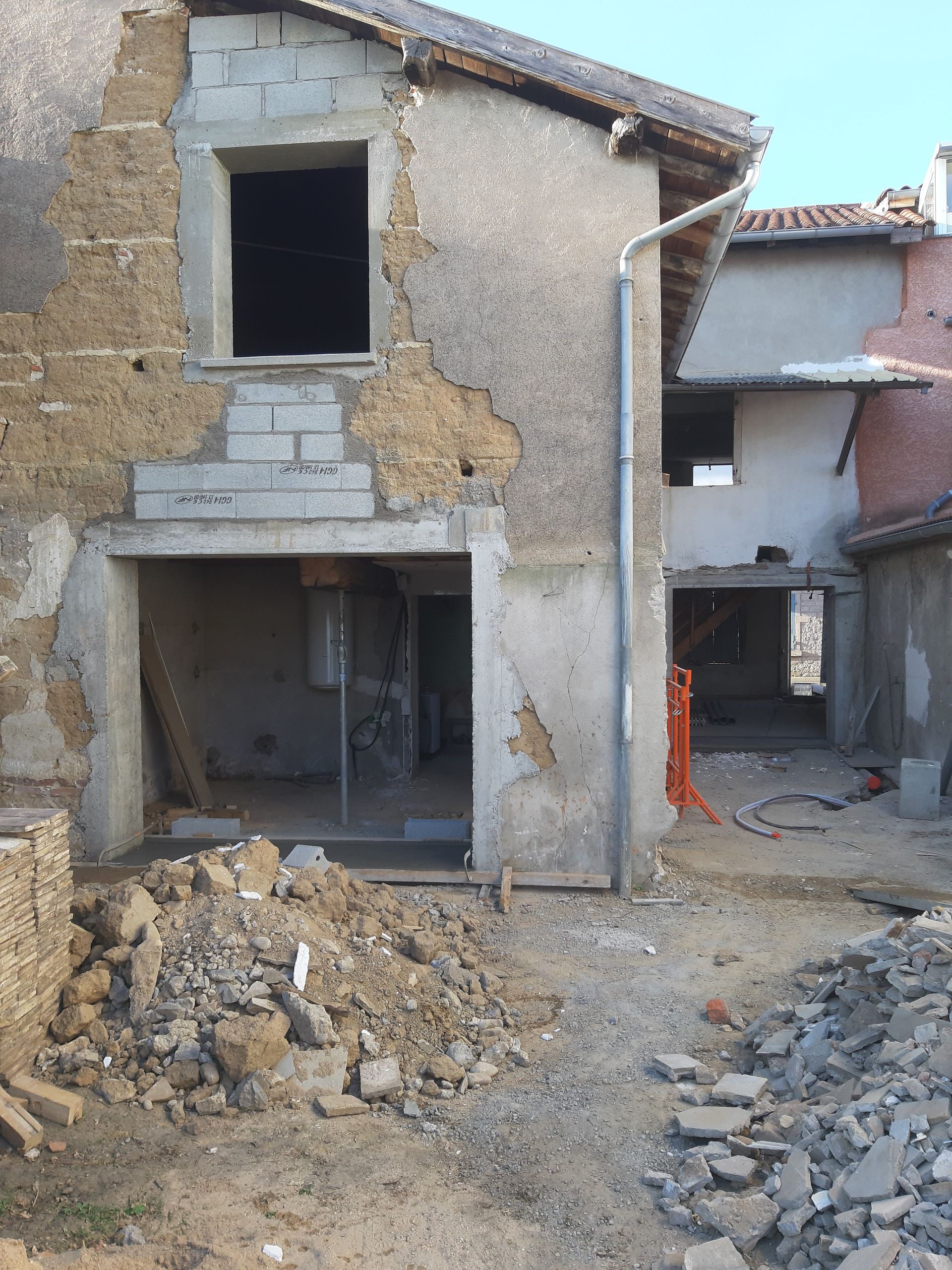 Vieille maison endommagée en cours de rénovation, avec un tas de gravats et des portes ouvertes dans une ruelle étroite.