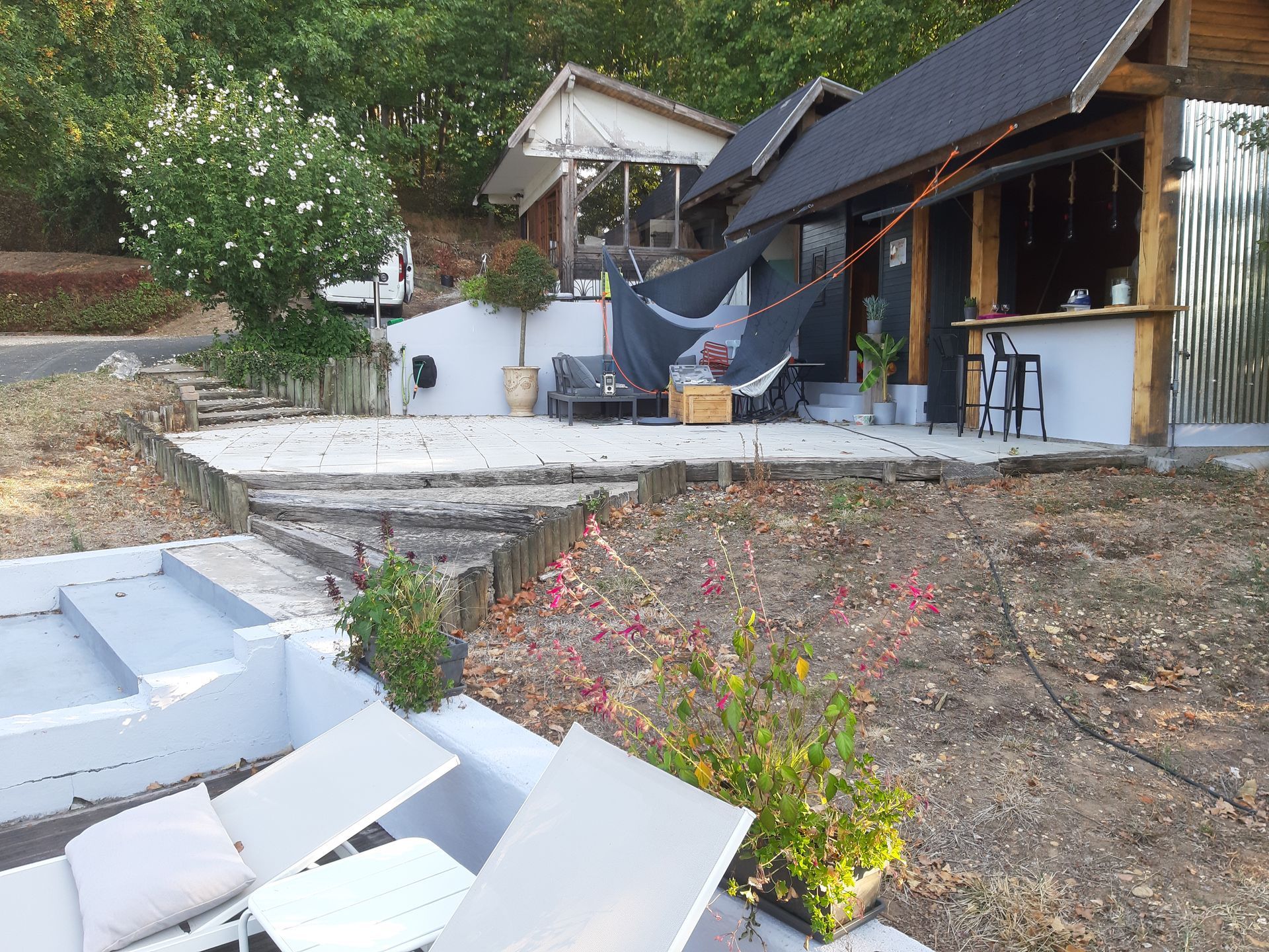 Terrasse avec chaises longues blanches, marches en pierre et maison à flanc de colline avec panneaux solaires et plantes