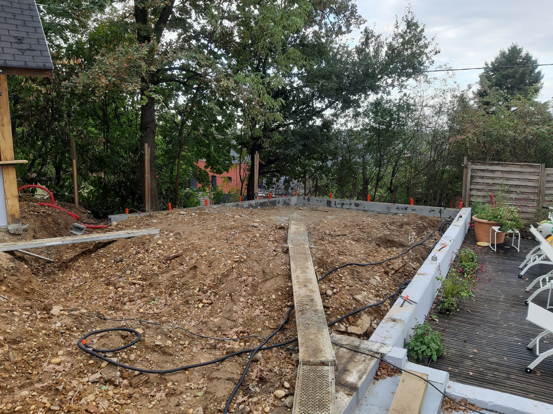 Zone de construction dans la cour arrière avec de la terre, une bordure en bois et des meubles de jardin près des arbres