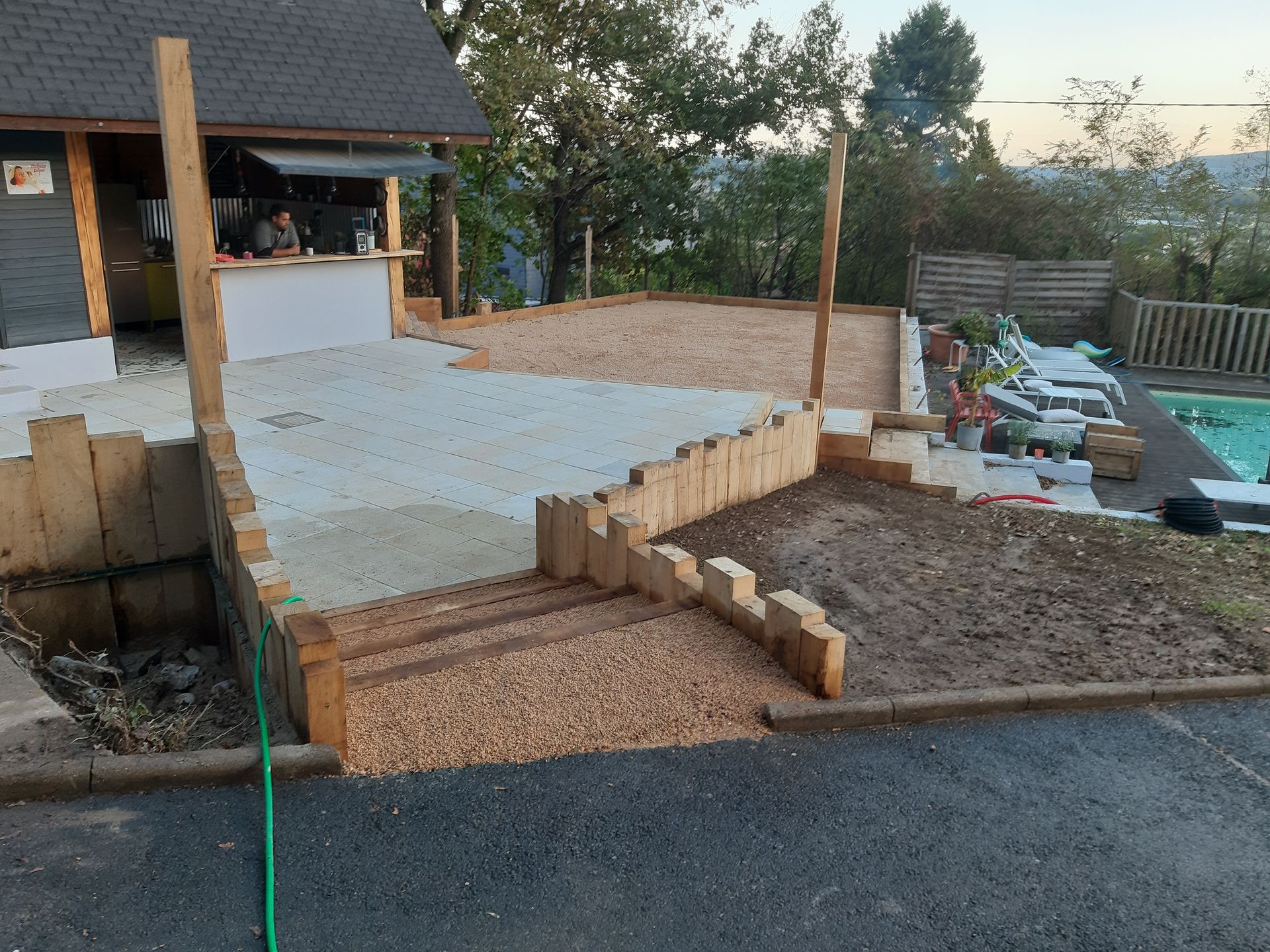 Terrasse arrière avec dalle de béton, marches en gravier et potager surélevé à côté d'une terrasse.