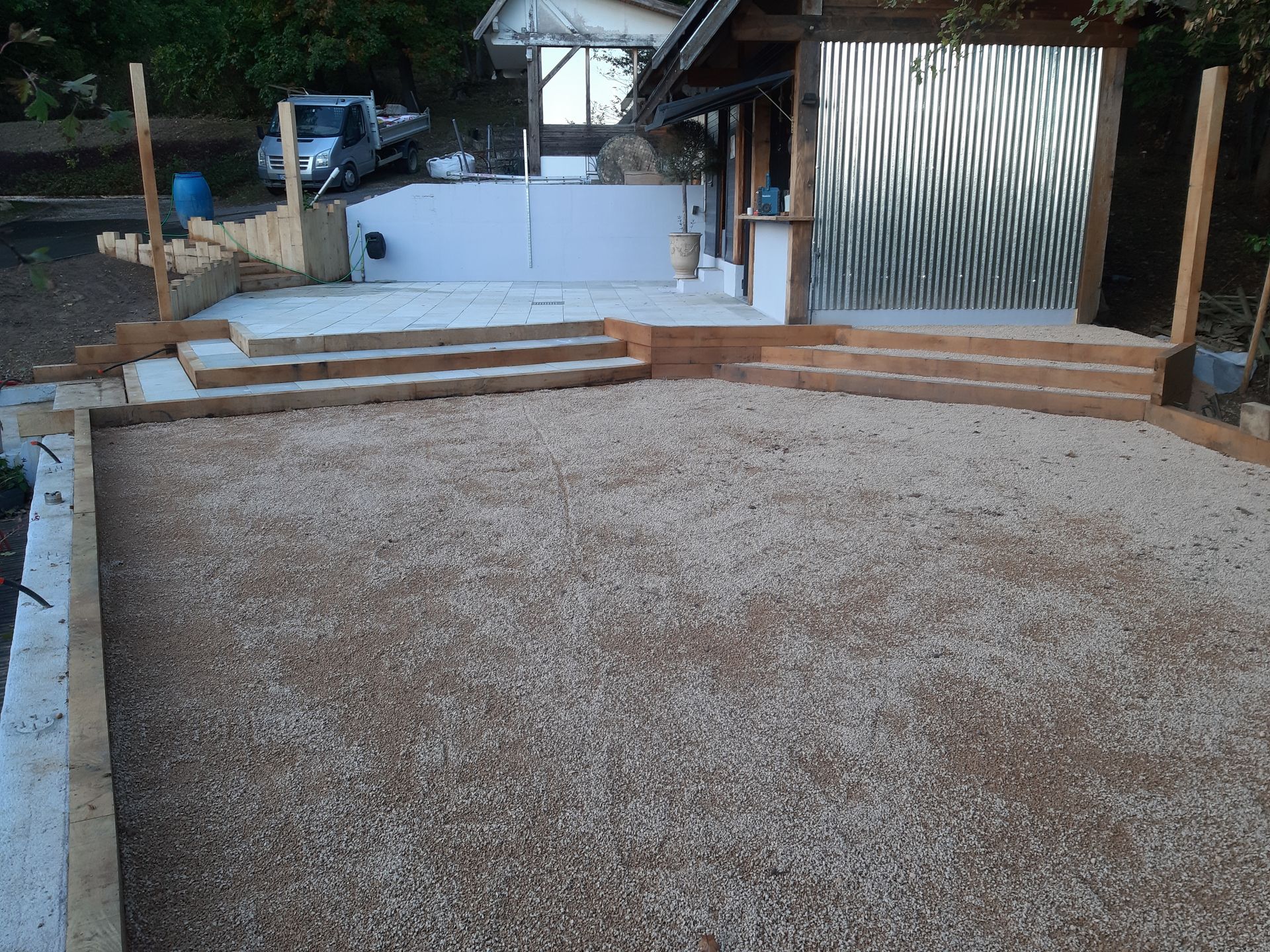 Terrasse extérieure en construction avec sol en gravier, coffrages en bois et petit muret de soutènement blanc.