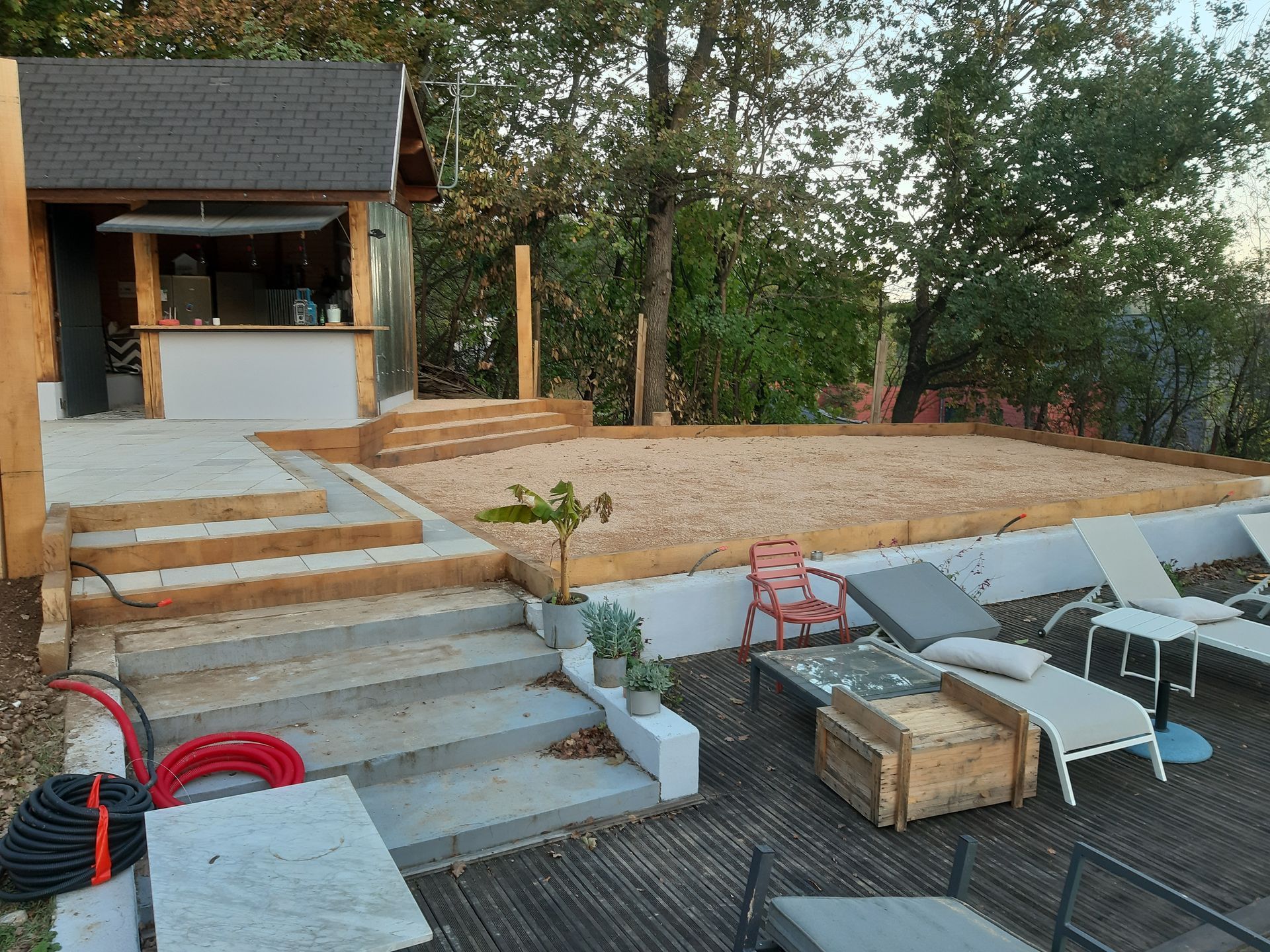 Terrasse extérieure avec escalier menant à un petit pavillon, chaises longues et un espace feu de camp en pierre