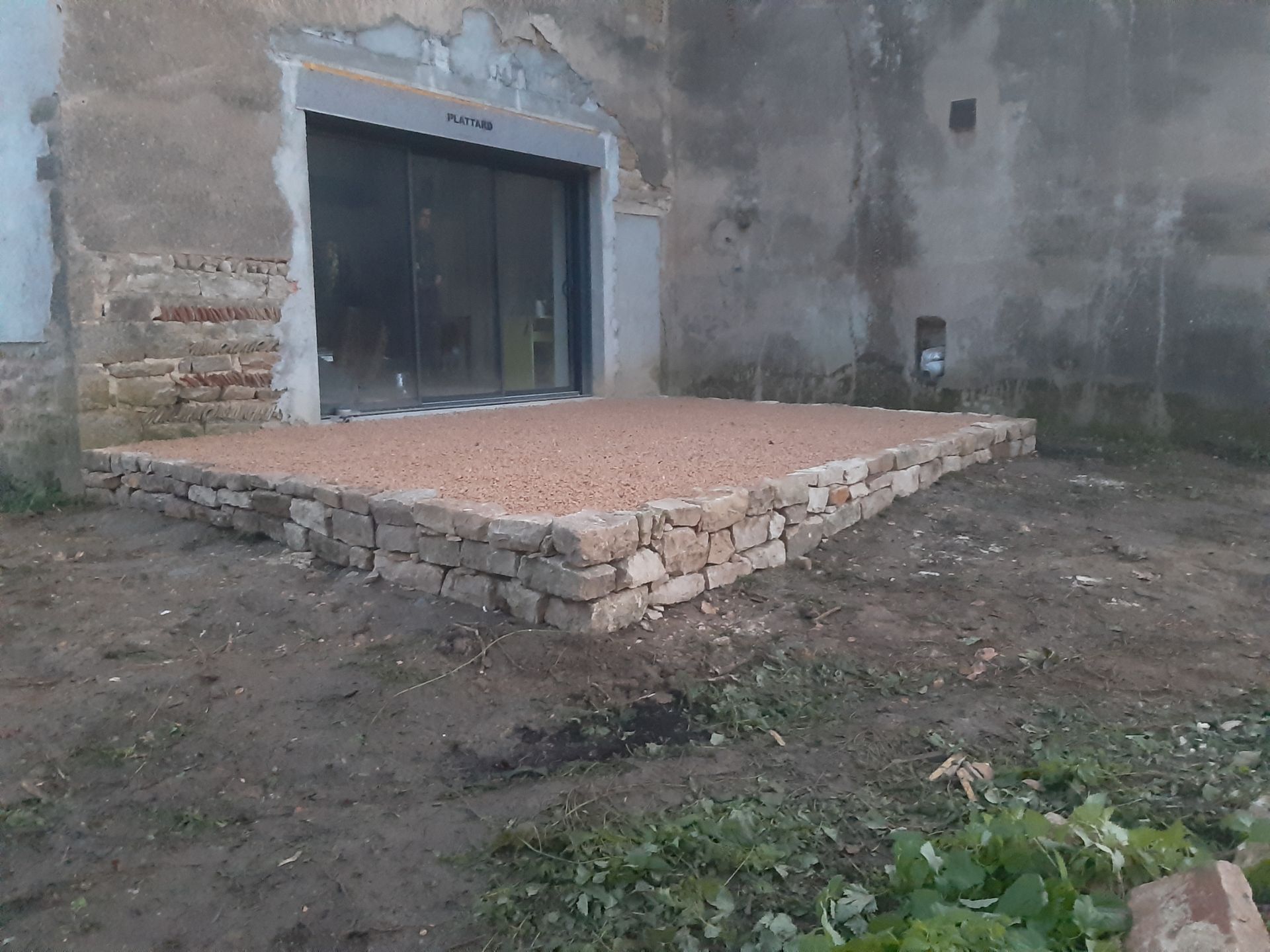 Terrasse en graviers rouges bordées de pierres devant une baie coulissante de maison.