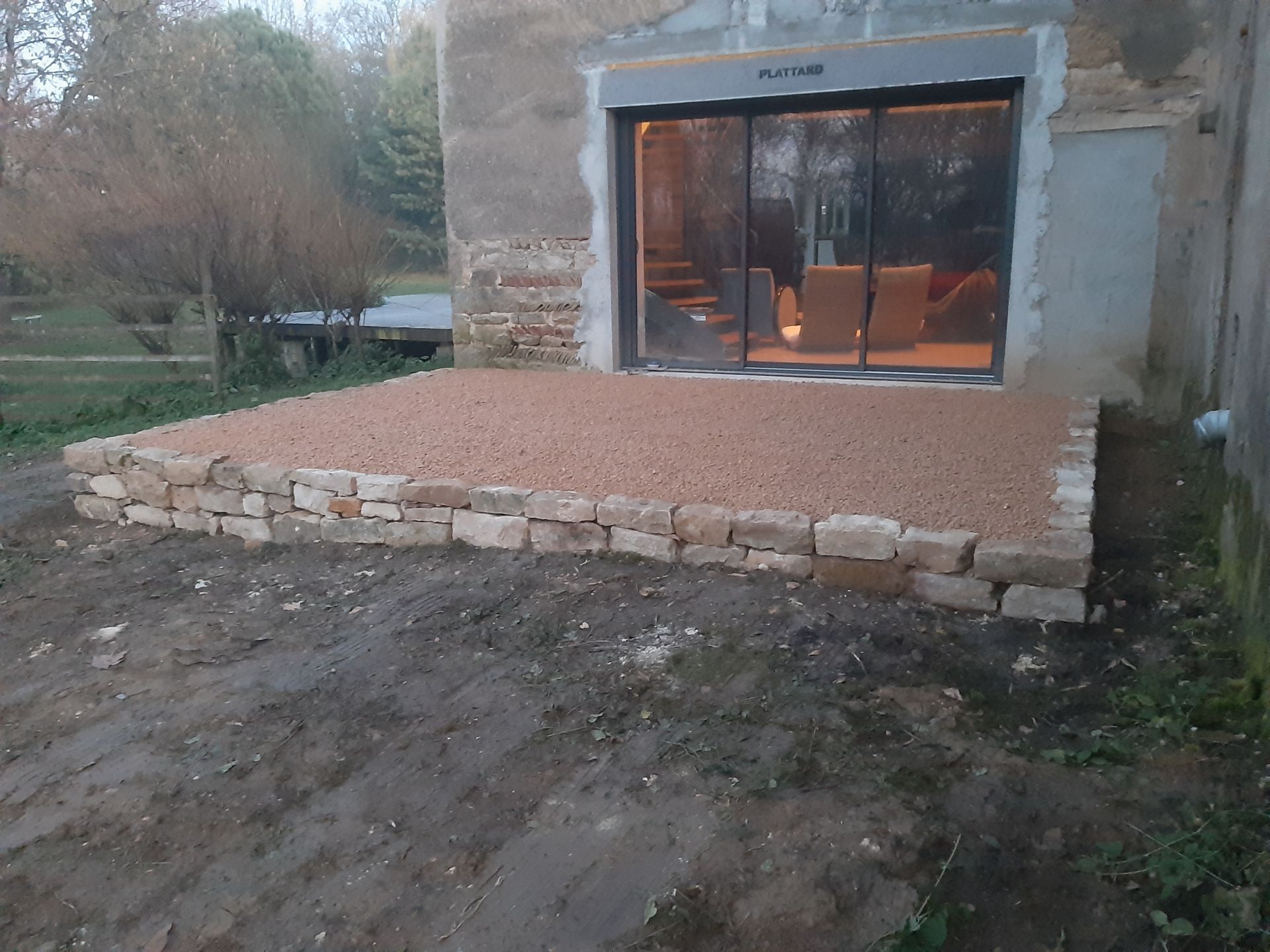 Terrasse en graviers rouges bordée de pierres devant une baie coulissante de maison en rénovation