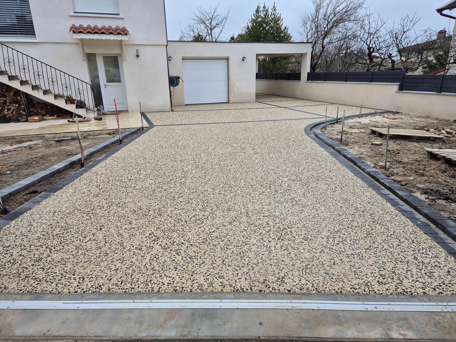 Allée de gravier menant à une maison avec garage et jardin nu sous un ciel dégagé