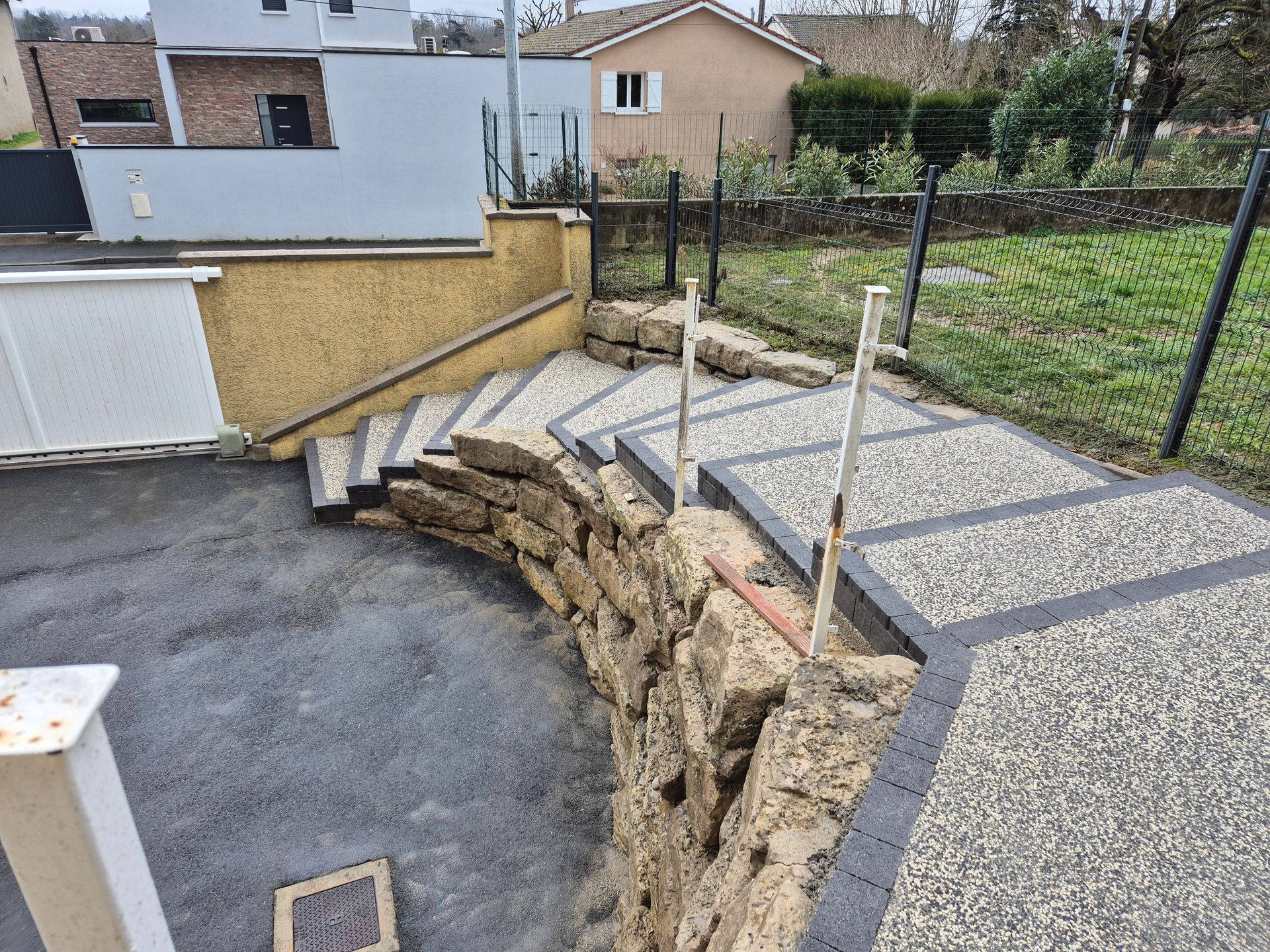 Aménagement d'une cour arrière avec un mur et marches en béton à côté d'une terrasse en gravier et d'une pente gazonnée.