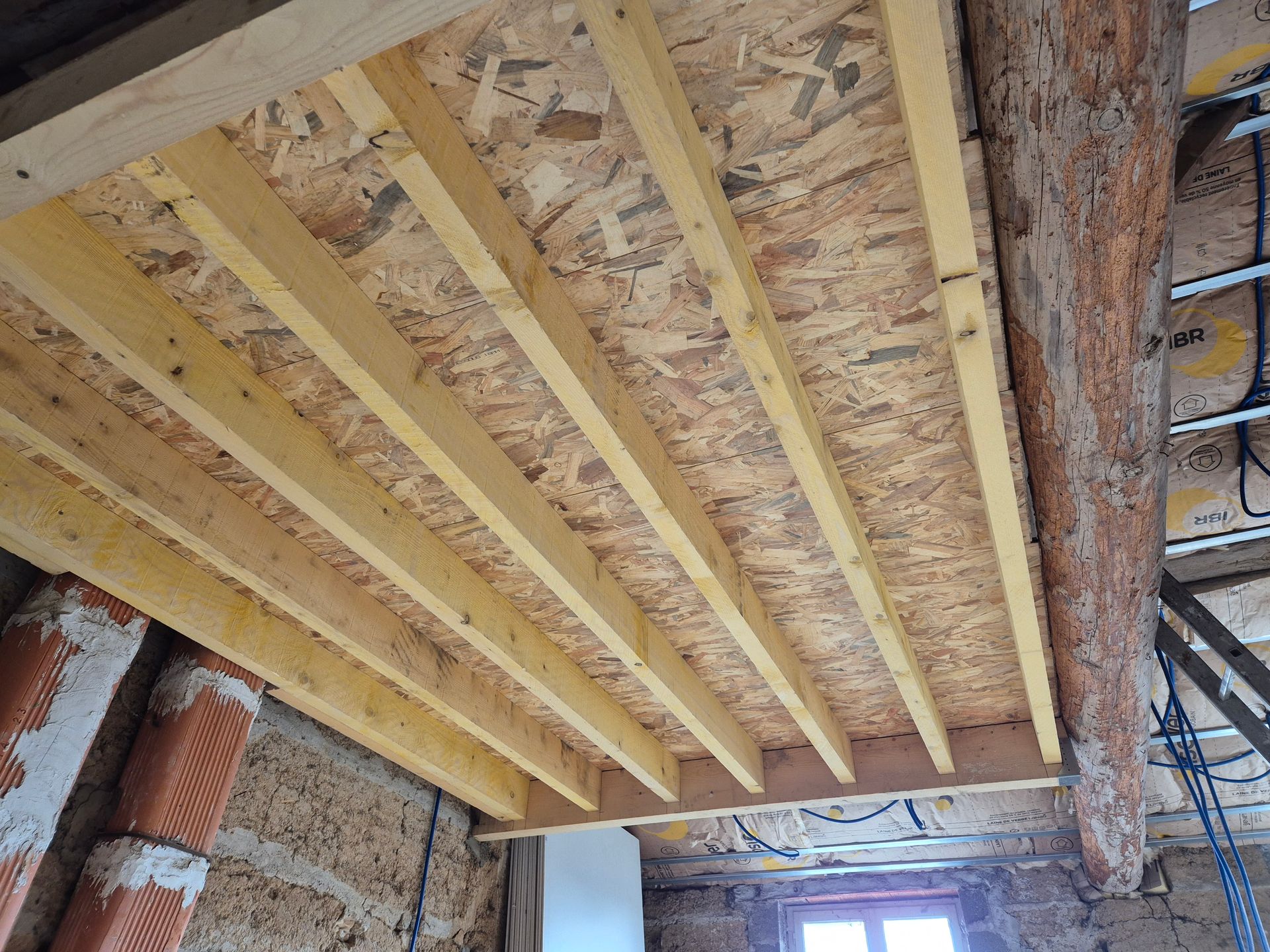 Charpente apparente du plafond en bois avec panneaux isolants dans un intérieur en construction, non fini