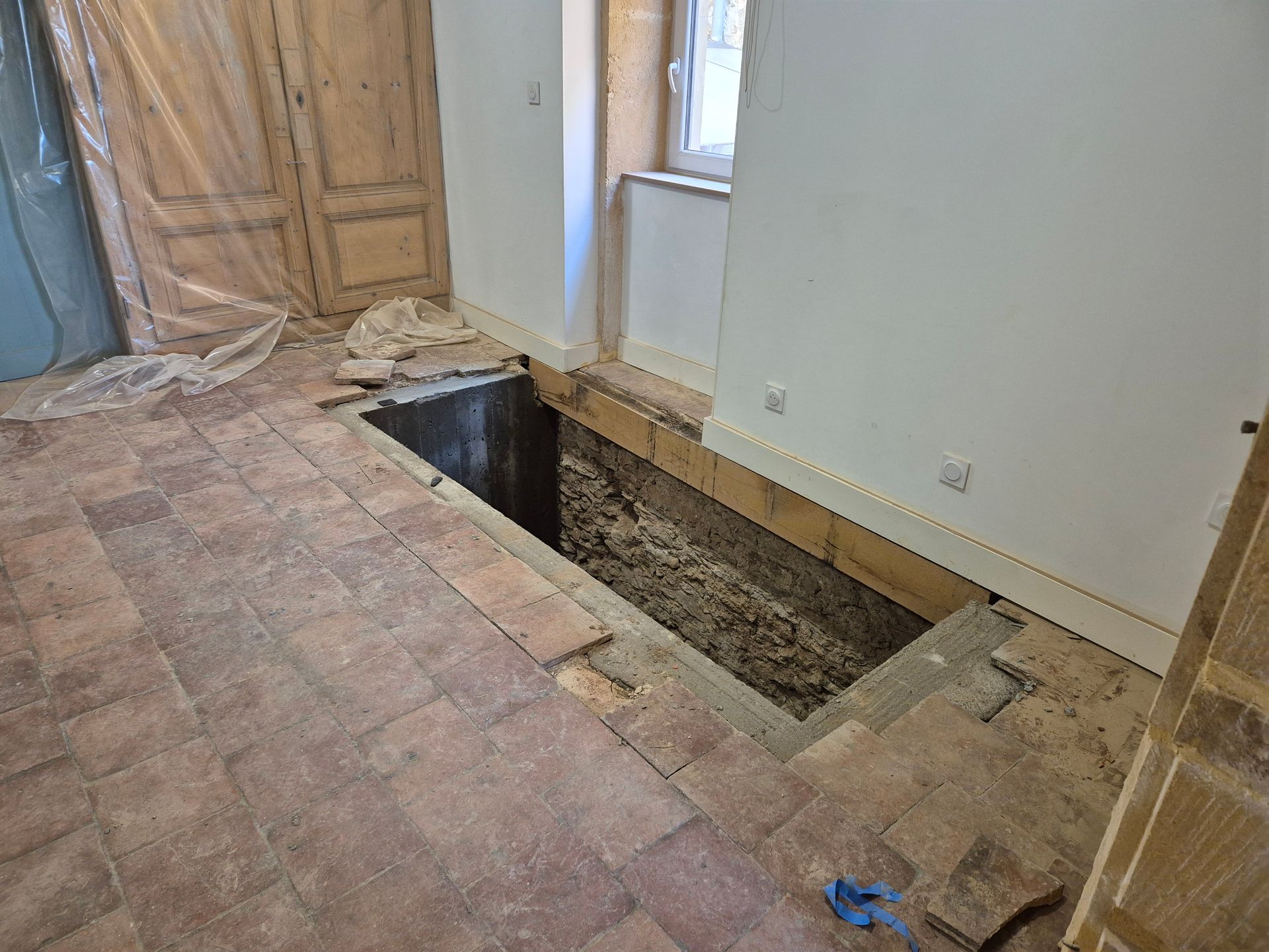 Chantier de rénovation avec une découpe rectangulaire dans le sol laissant apparaître le sous-plancher