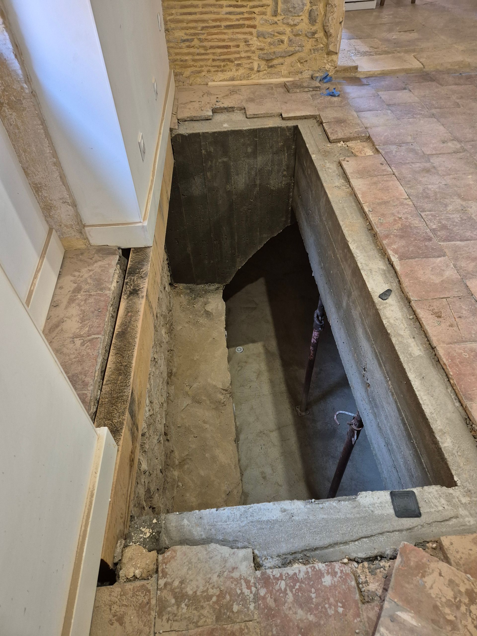 Trappe d'accès au sol dans un couloir, révélant une cage d'escalier sombre ou une ouverture vers un sous-sol.