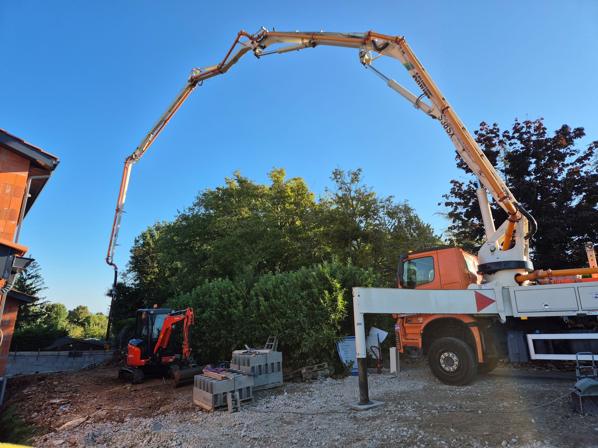 Camion de chantier à longue flèche pompant du béton sur un site bordé d'arbres et d'une maison
