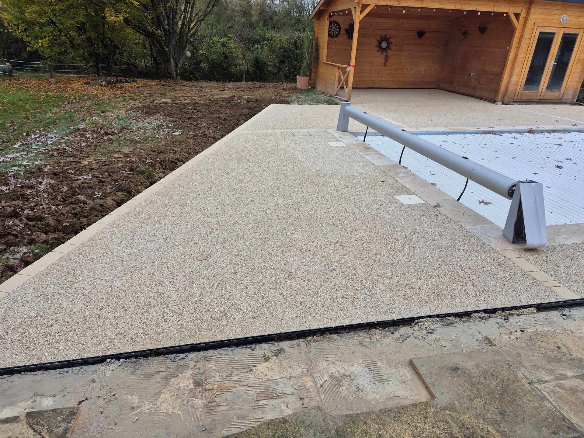 Terrasse recouverte de gravier avec une petite rampe en béton menant à l'entrée d'une maison en bois.