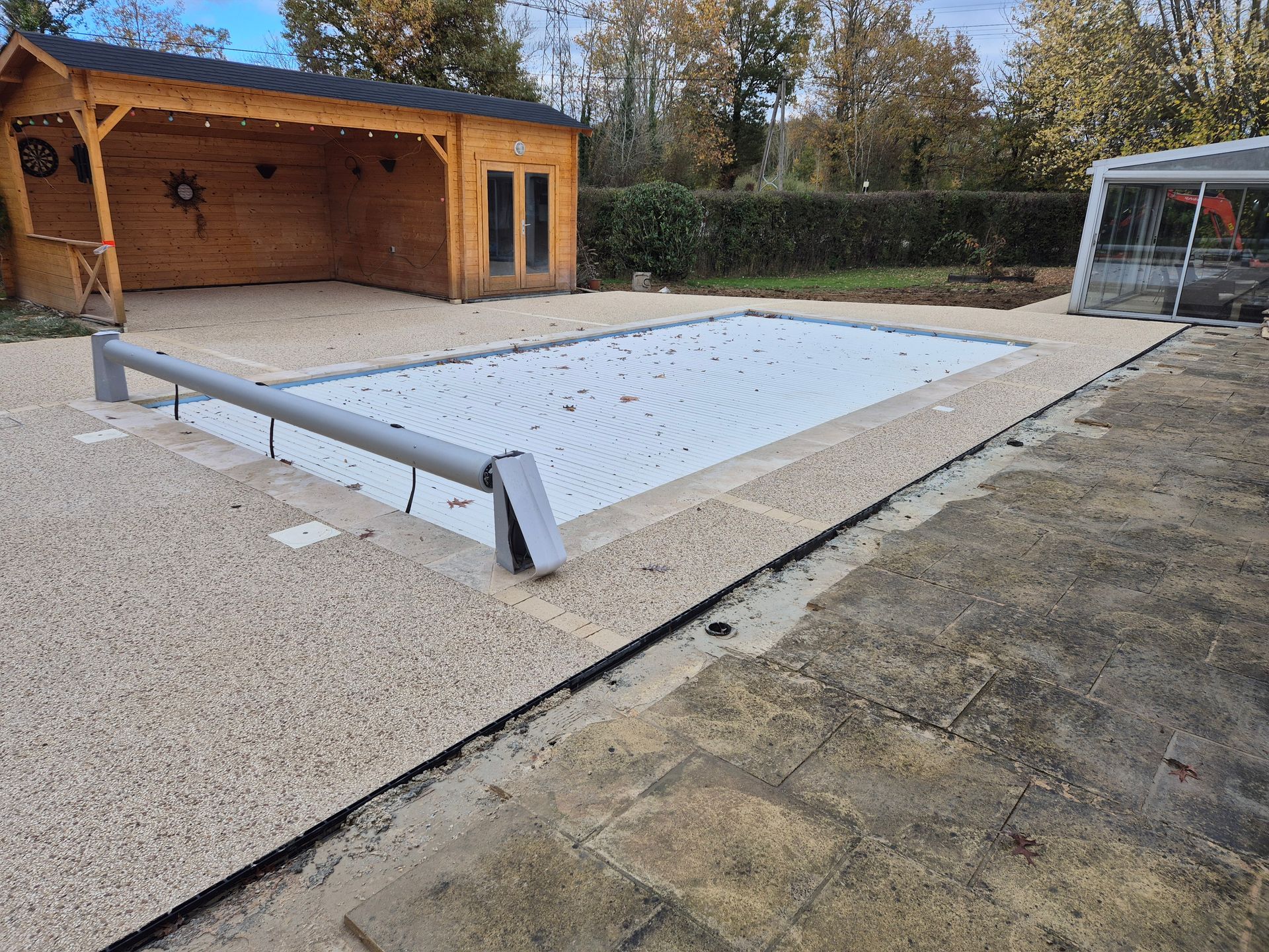 Couverture de piscine extérieure dans une cour arrière, à côté d'un abri de jardin en bois et d'une terrasse.