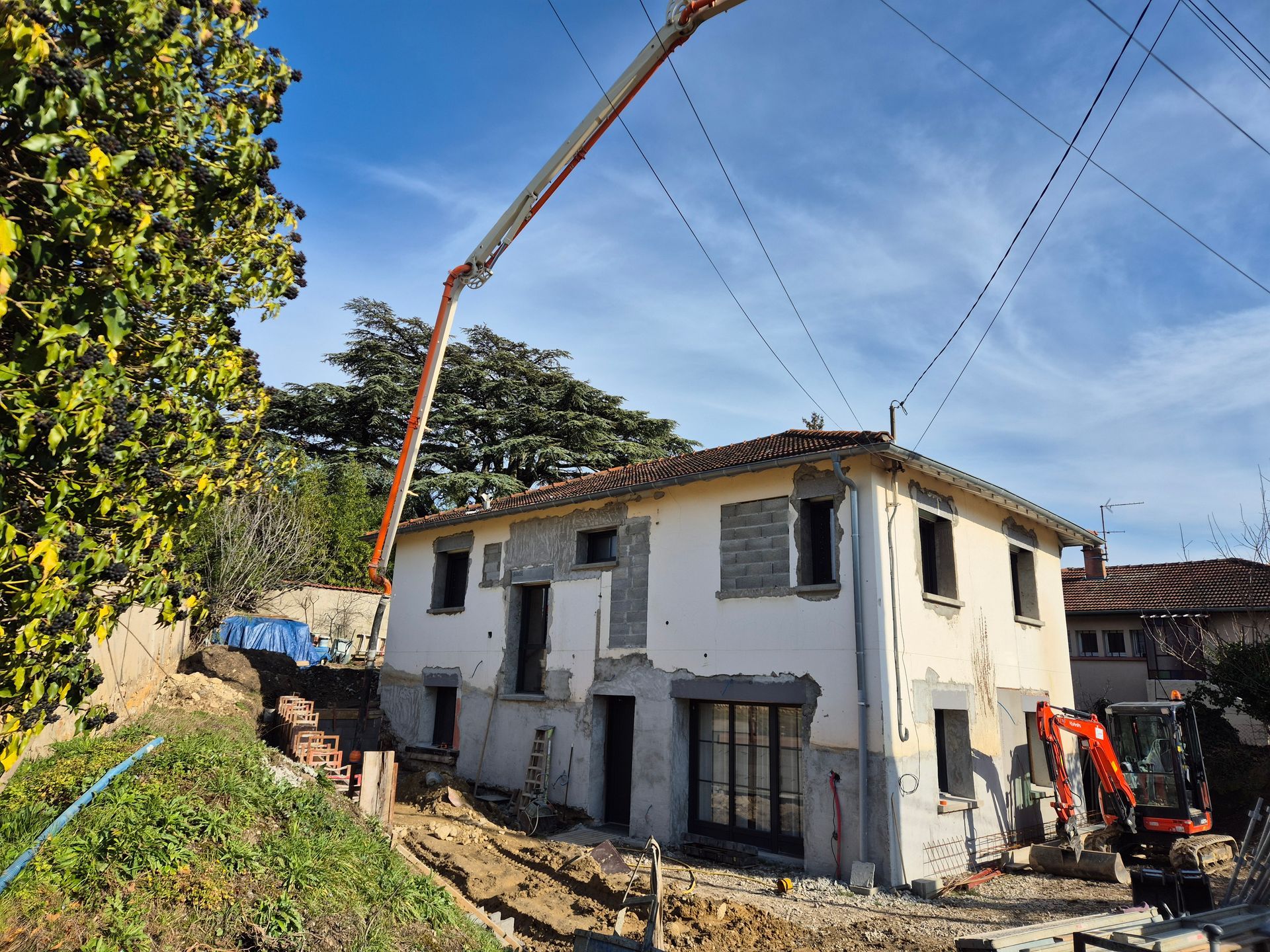 Maison blanche partiellement rénovée avec une grue et une excavatrice sur une colline sous un ciel bleu