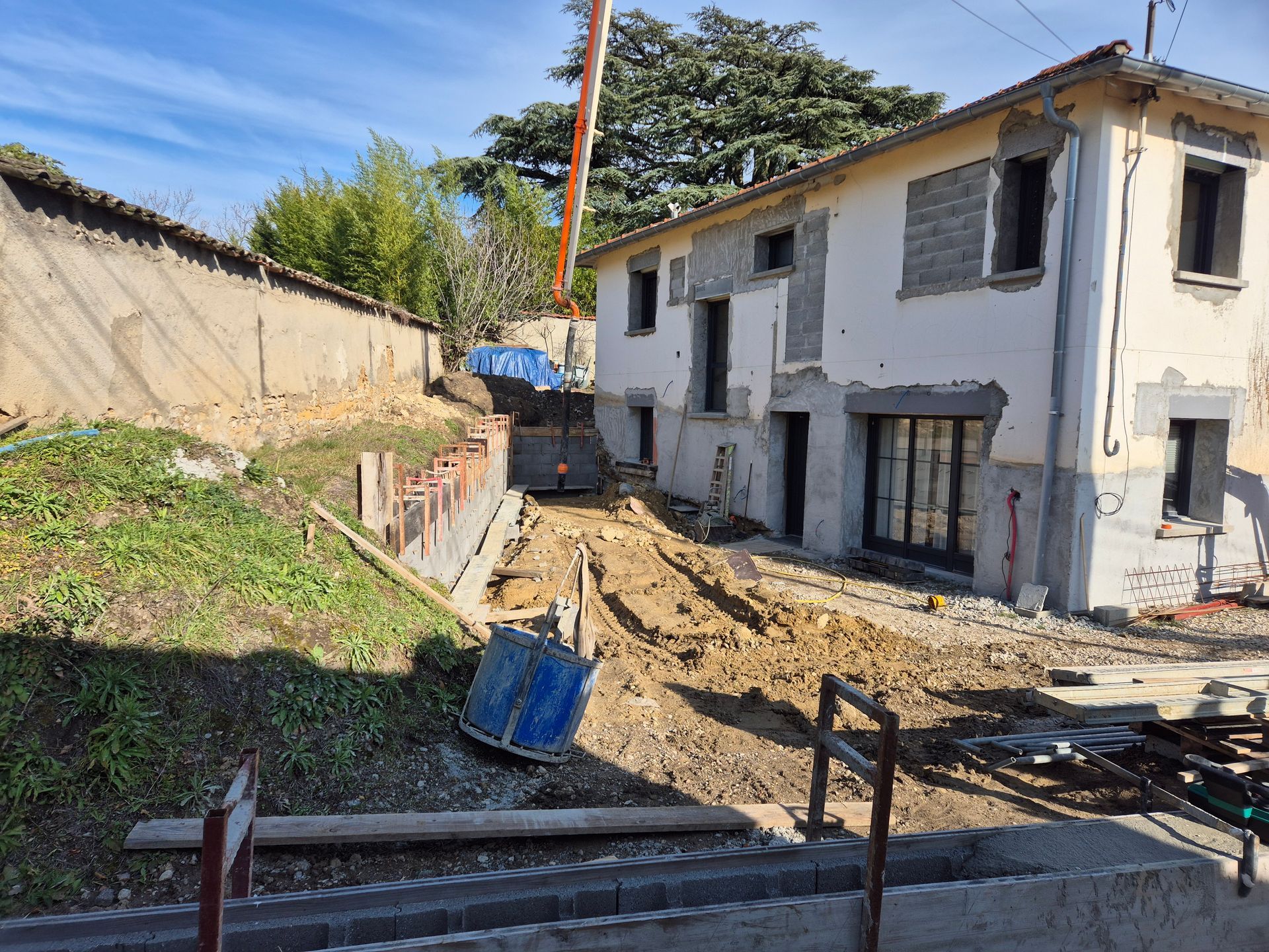 Terrain résidentiel en construction avec une maison blanche partiellement démolie et un sol en terre excavée