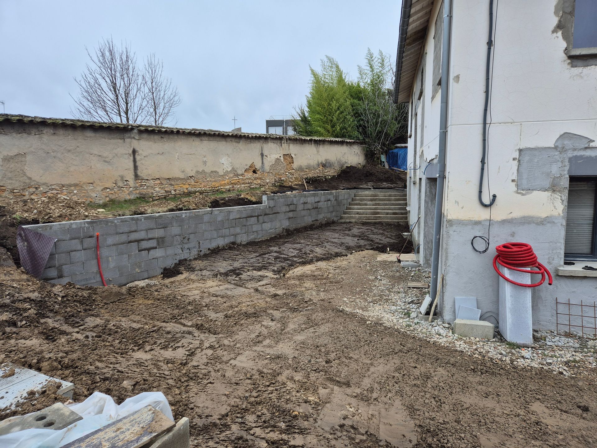 Cour arrière avec un mur de soutènement et un enrouleur de tuyau rouge.