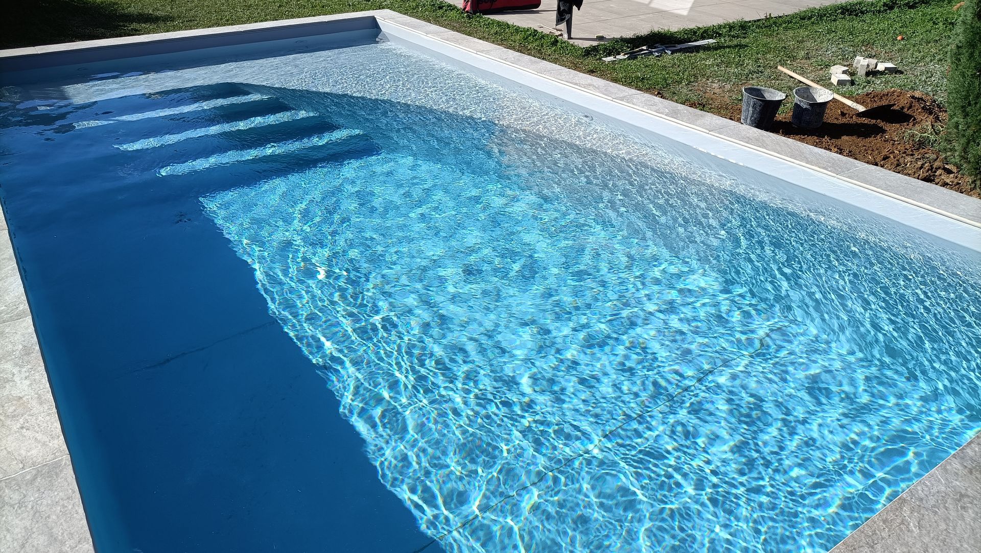 Une piscine d'un bleu limpide aux eaux frémissantes, bordée d'une pelouse et d'un parterre de fleurs.