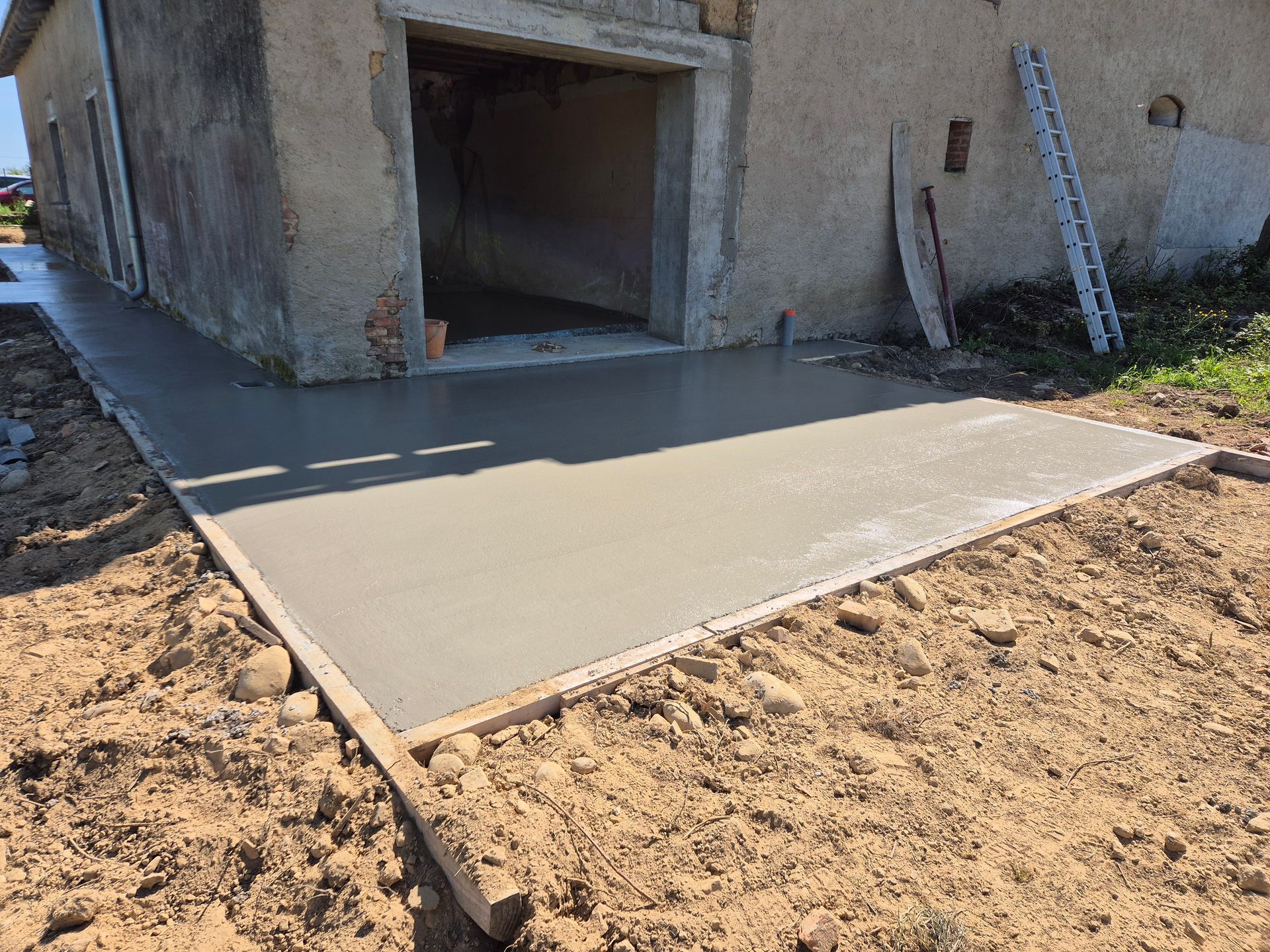 Dalle de béton frais devant l'entrée d'un bâtiment inachevé, entourée de terre.