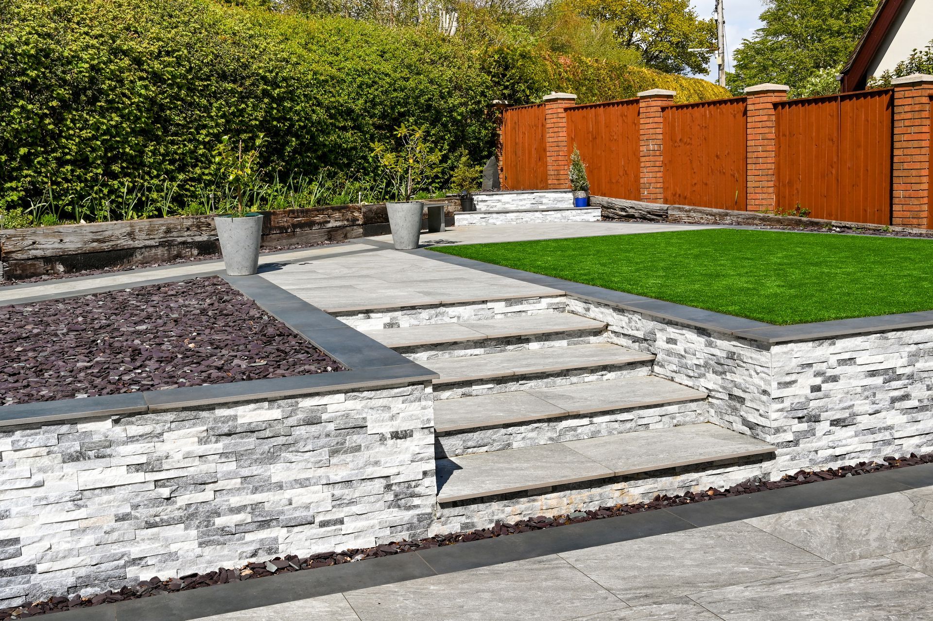 Patio paysager moderne avec marches en pierre, parterres de gravier, pelouse verte et clôture en bois