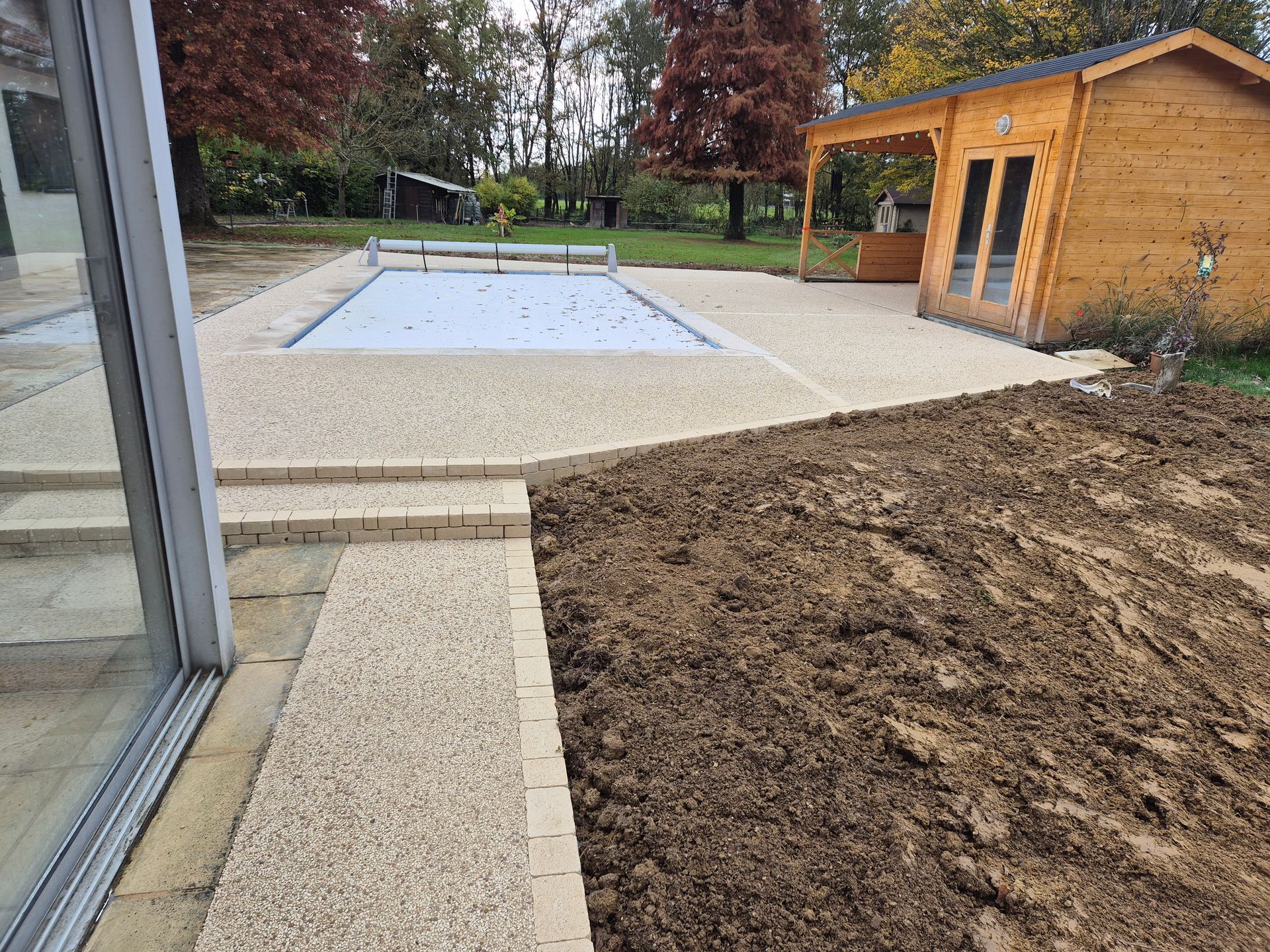 Terrasse avec piscine couverte, abri en bois, allée en pierre et terre fraîche au premier plan.