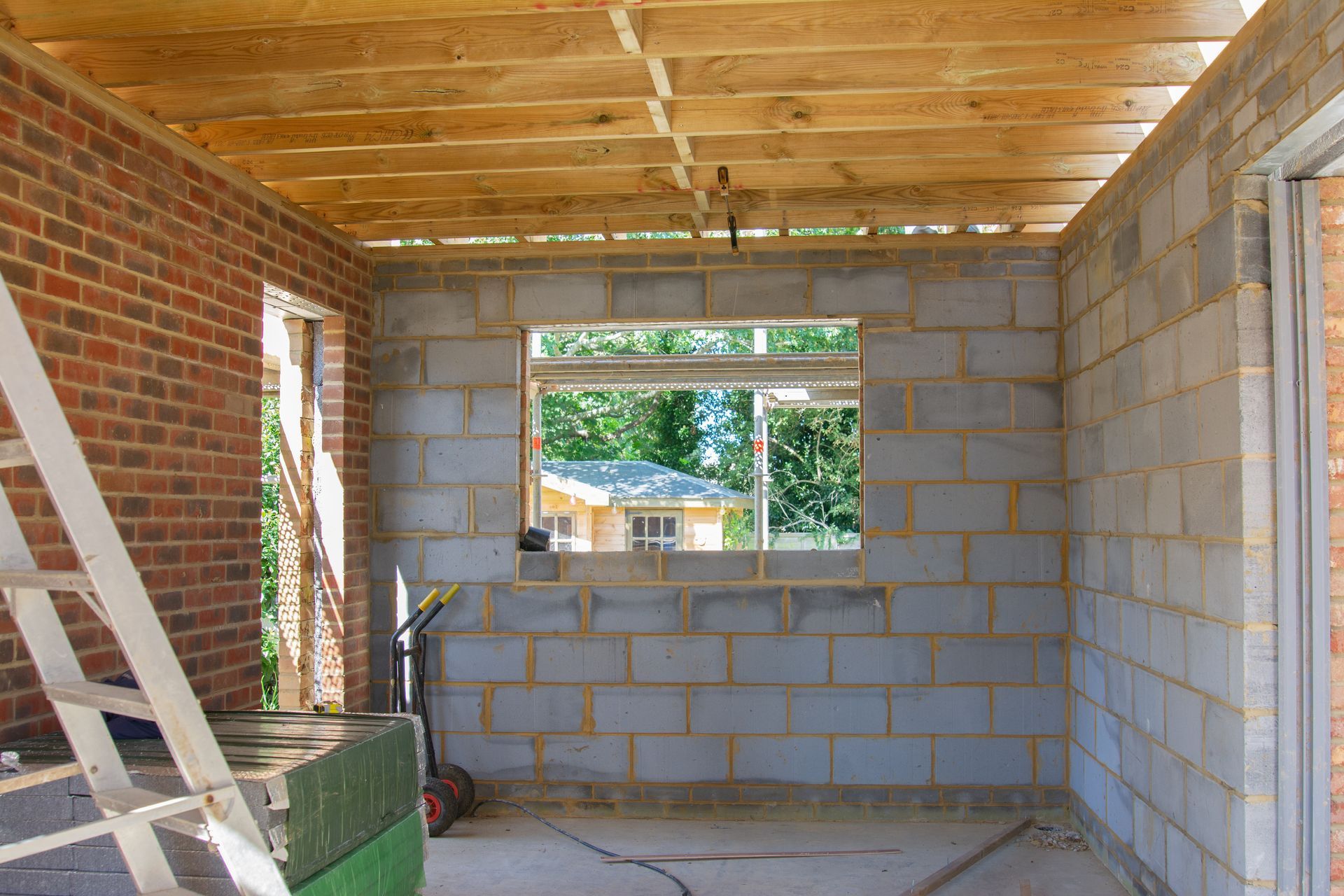 Pièce partiellement construite avec murs en parpaings, charpente en bois, fenêtre et une échelle.