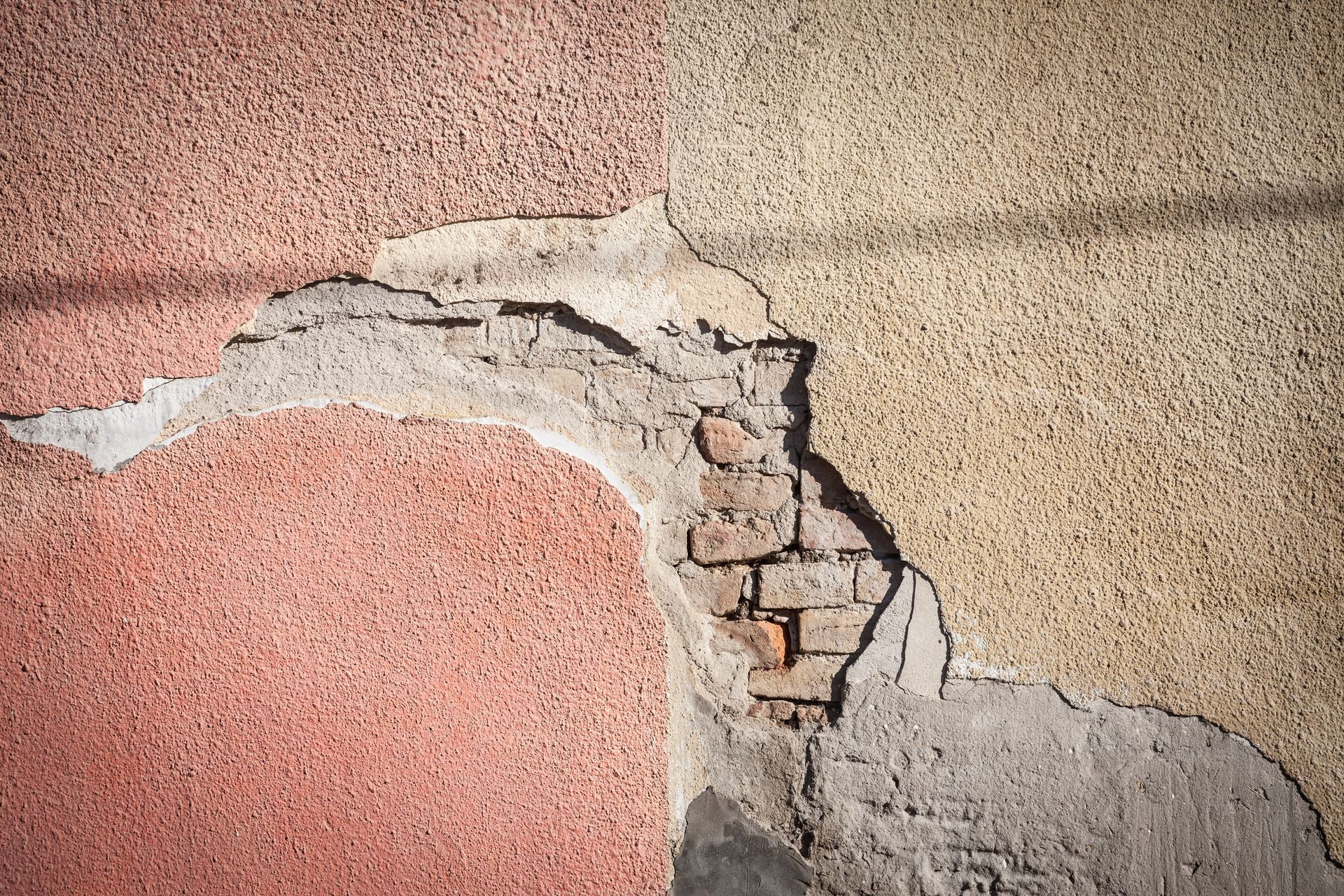 Mur en stuc fissuré, la peinture rose et beige s'écaillant et laissant apparaître la maçonnerie brute en dessous.