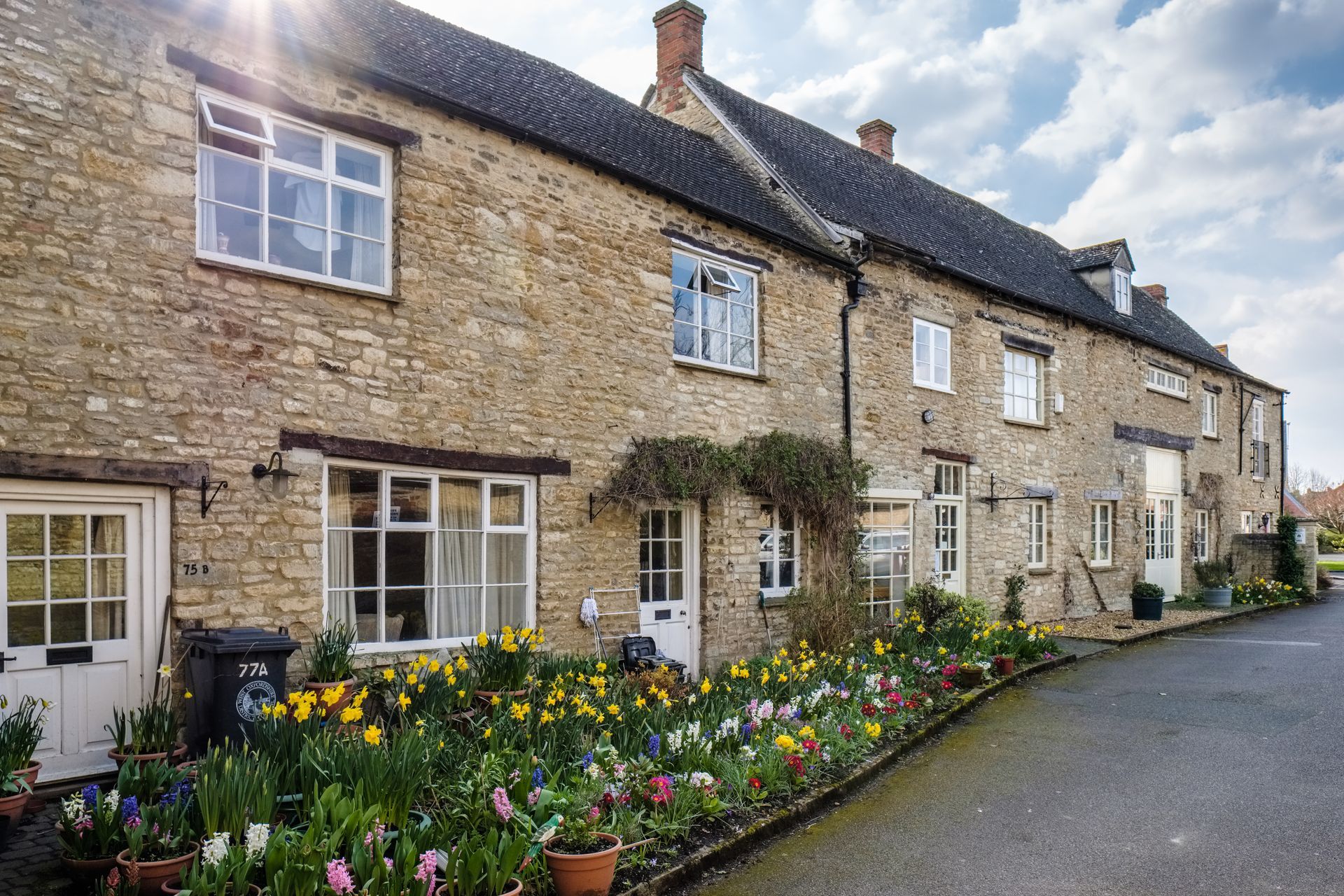 Rangée de maisons en pierre avec des jardins fleuris devant la façade, le long d'une ruelle de village tranquille.