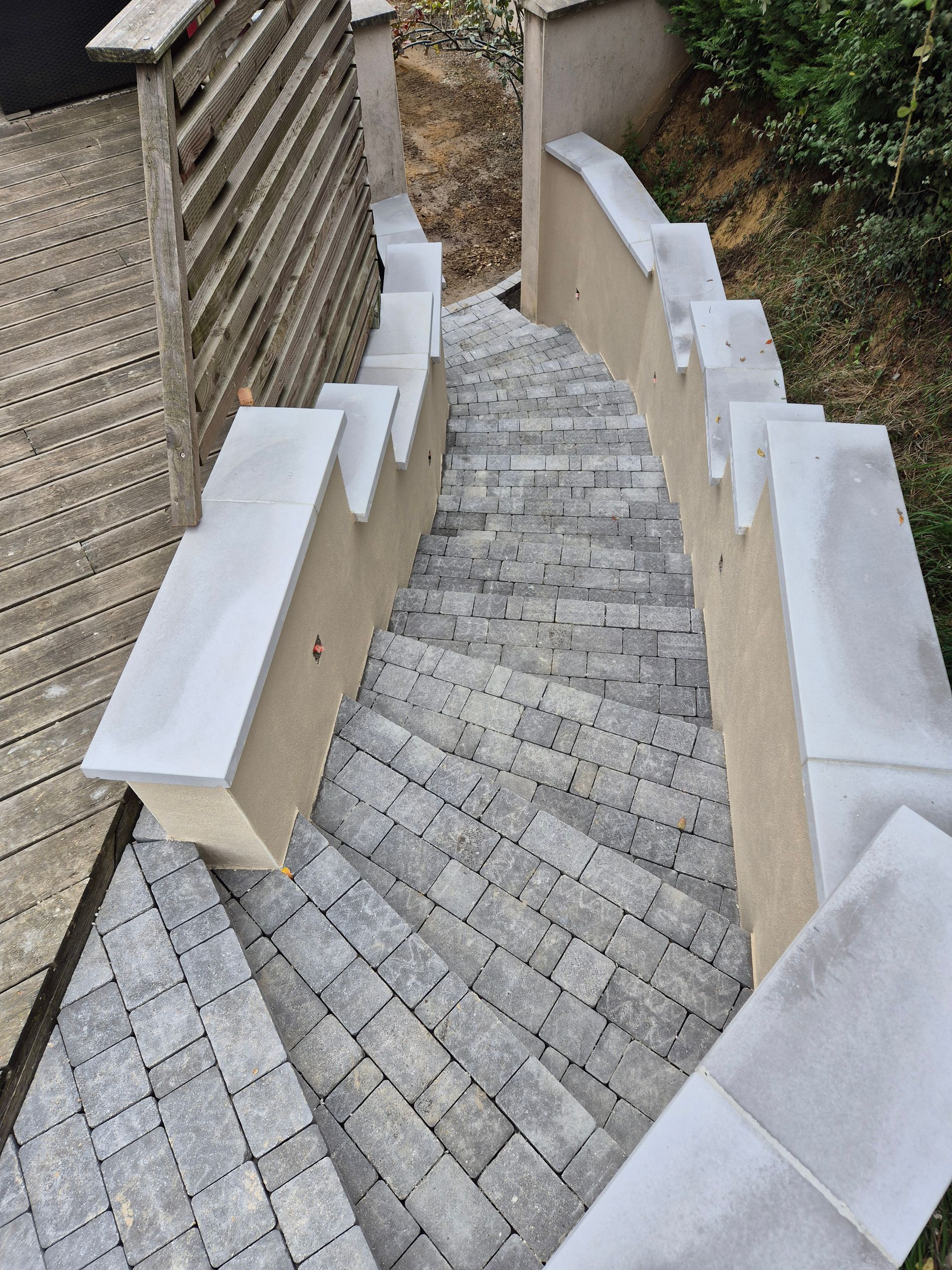 Escalier extérieur en pierre, aux murs beiges et aux rampes blanches, descendant la pente.