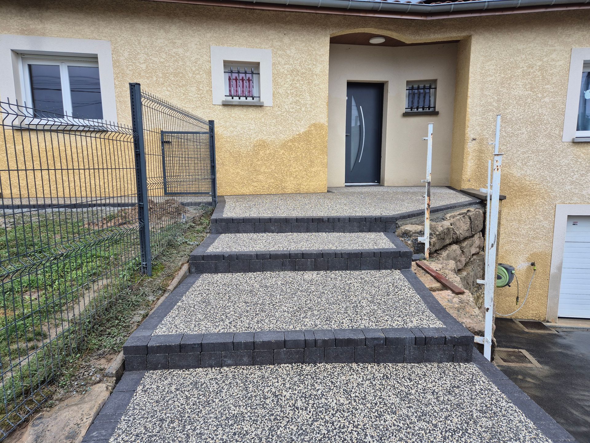Des marches en béton mènent à l'entrée d'une maison, bordée de chemins de gravier de chaque côté.