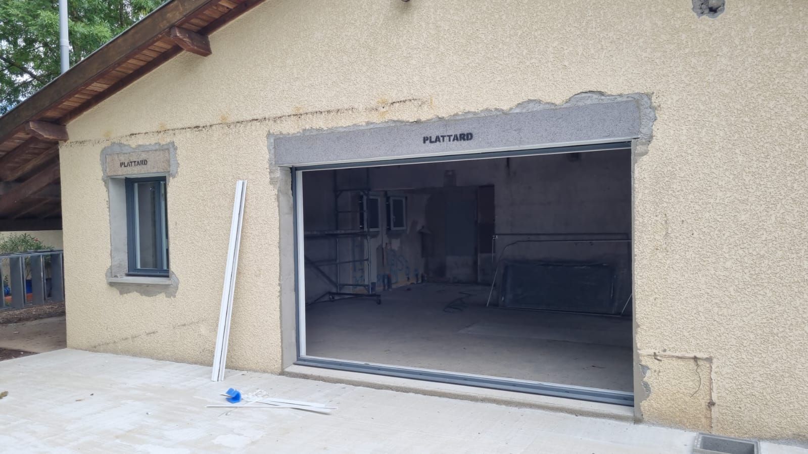 Entrée de type garage ouverte dans un bâtiment en stuc beige avec une structure en pierre et échelle