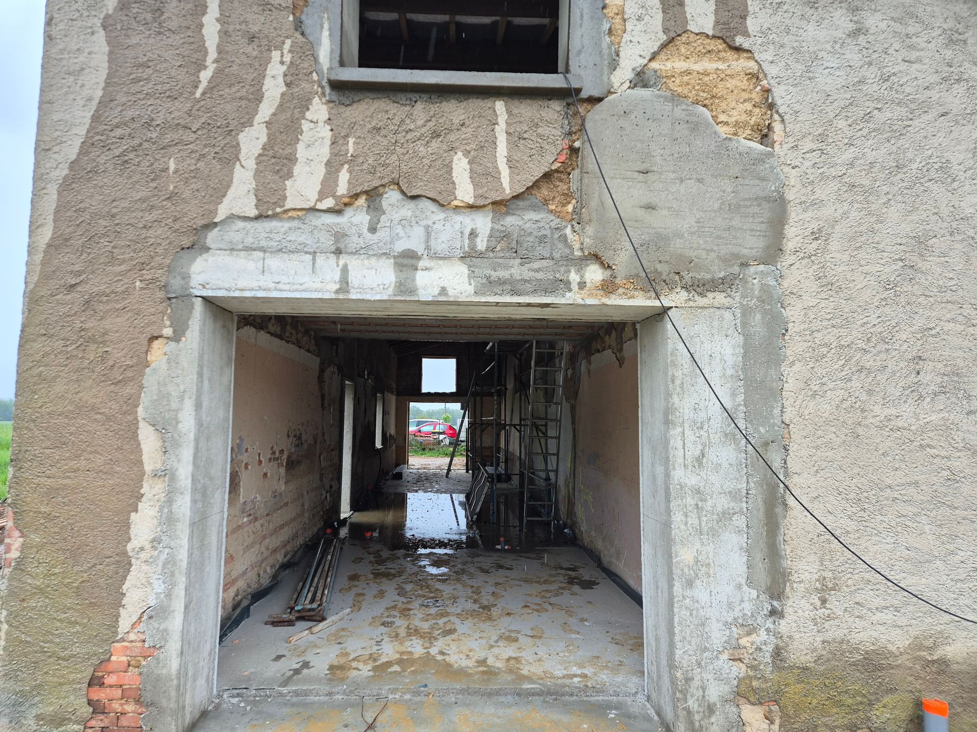 Passage en béton fissuré sous un bâtiment, avec des murs endommagés et une vue sur l'extérieur.