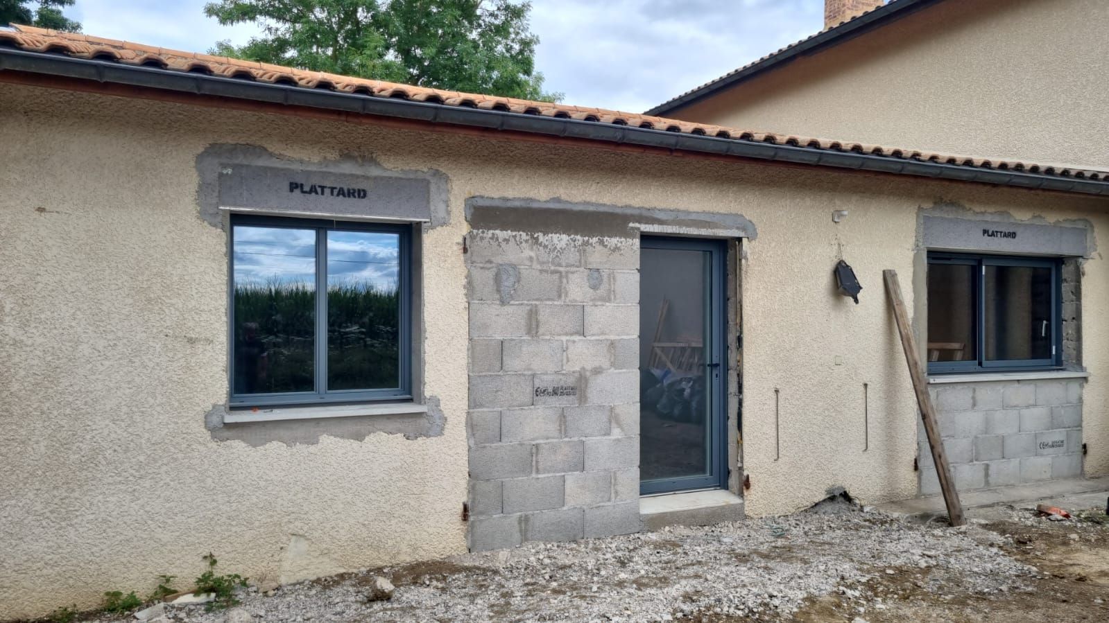 Extérieur d'une petite maison en stuc avec une porte centrale, des fenêtres et une cour en gravier.