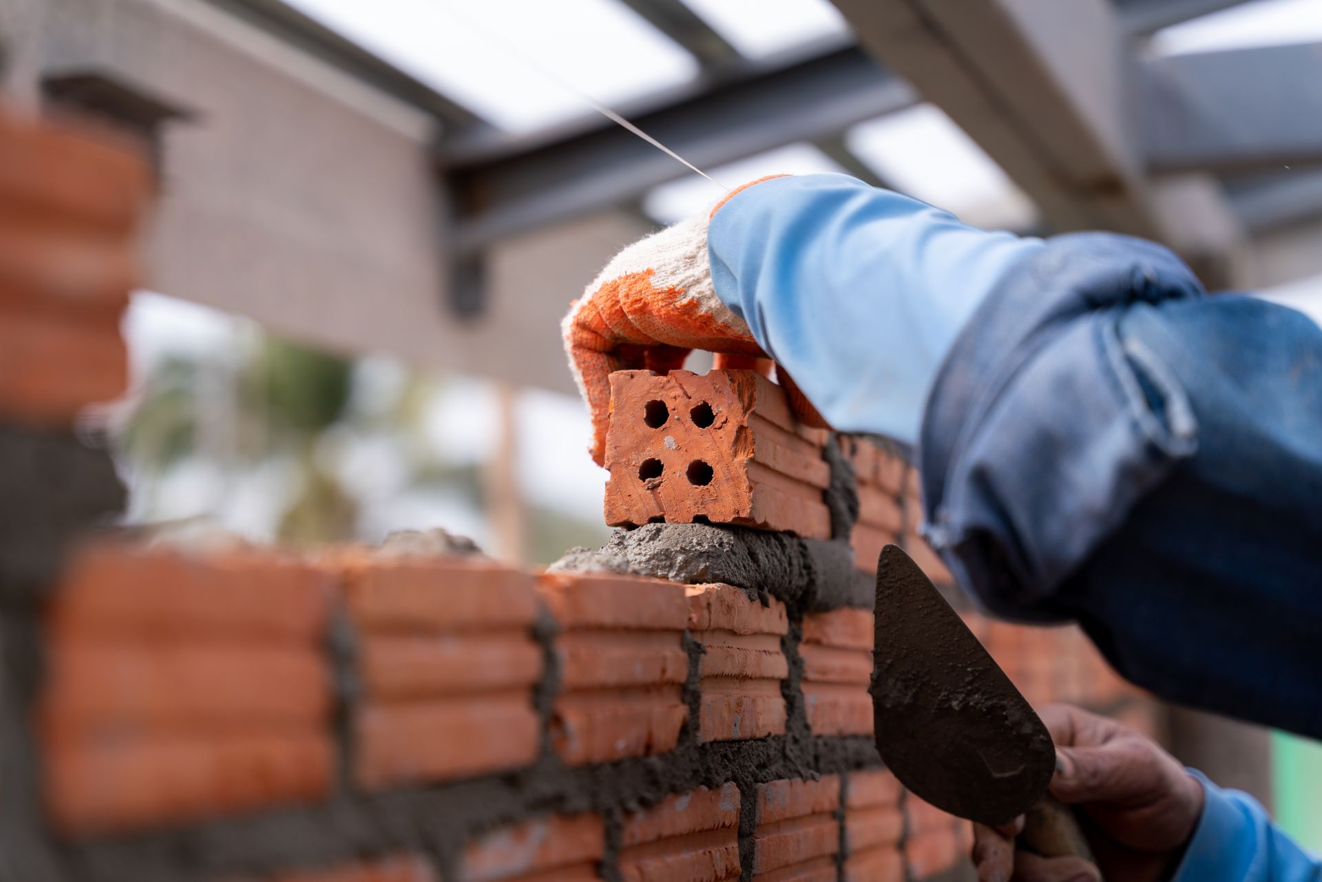 Des mains posent des briques à la truelle sur un mur de briques sur un chantier de construction.
