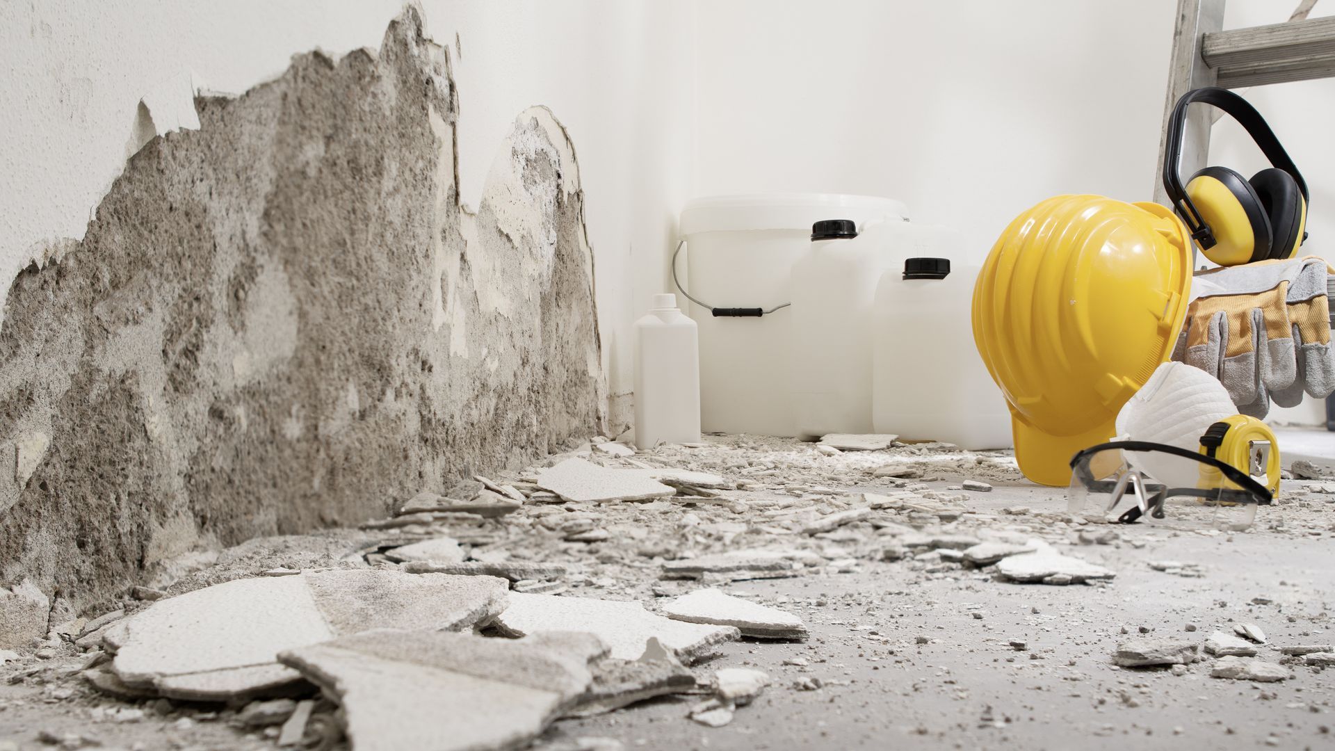 Pièce endommagée avec un mur qui s'écaille, des débris au sol, et un casque de chantier.