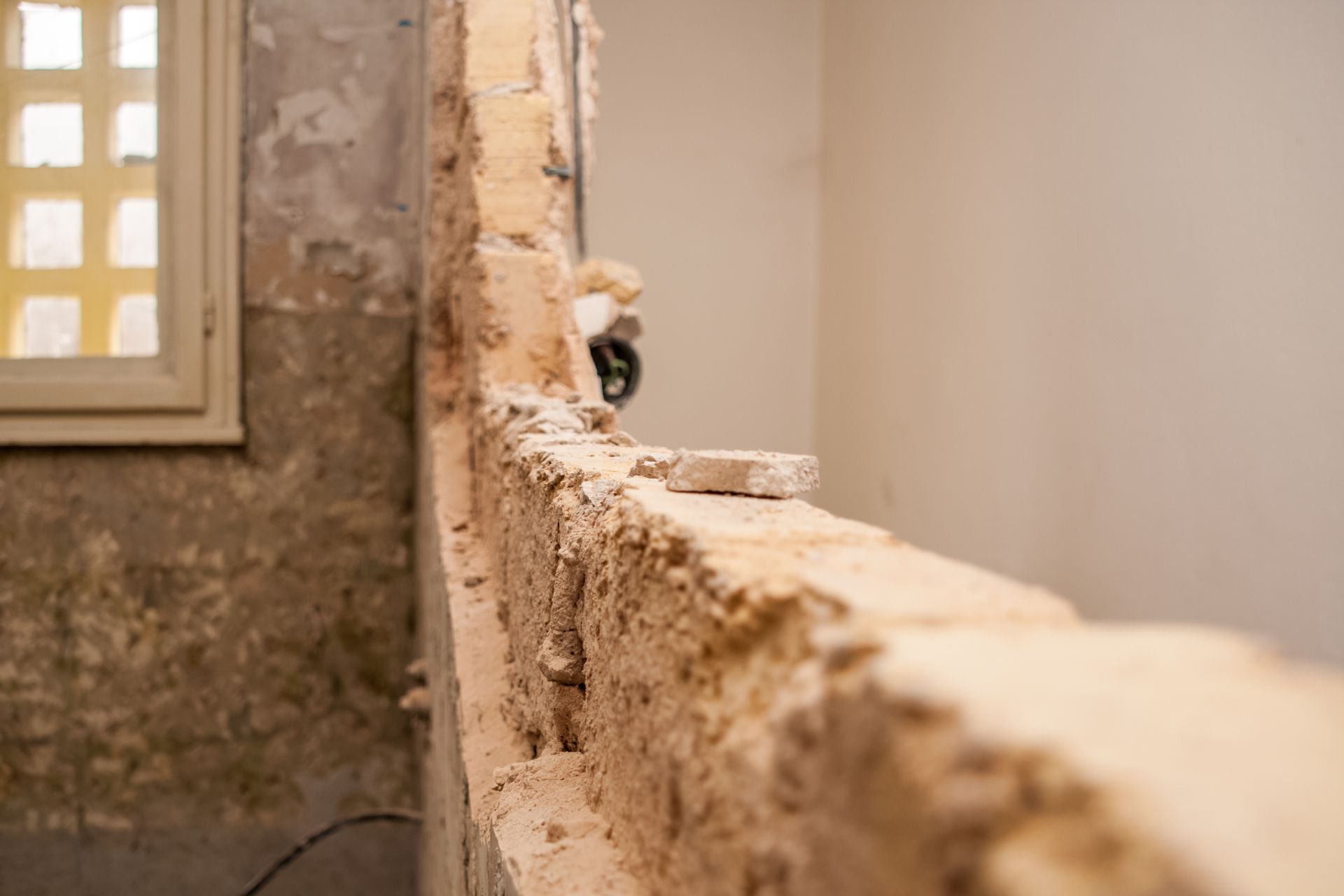 Vieux mur de pierre avec une fenêtre, d'où un petit chien jette un coup d'œil par-dessus le bord.