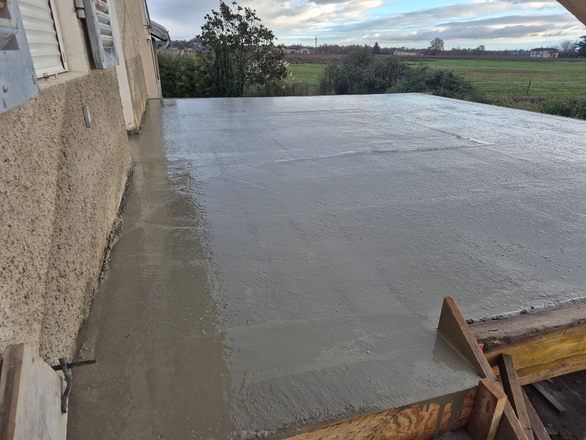 Dalle de béton fraîchement coulée à côté d'une maison et un ciel nuageux en arrière-plan.